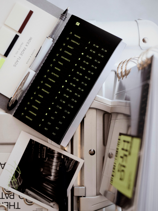 An open black sticker notebook, page flags and journaling card resting on a white suitcase.