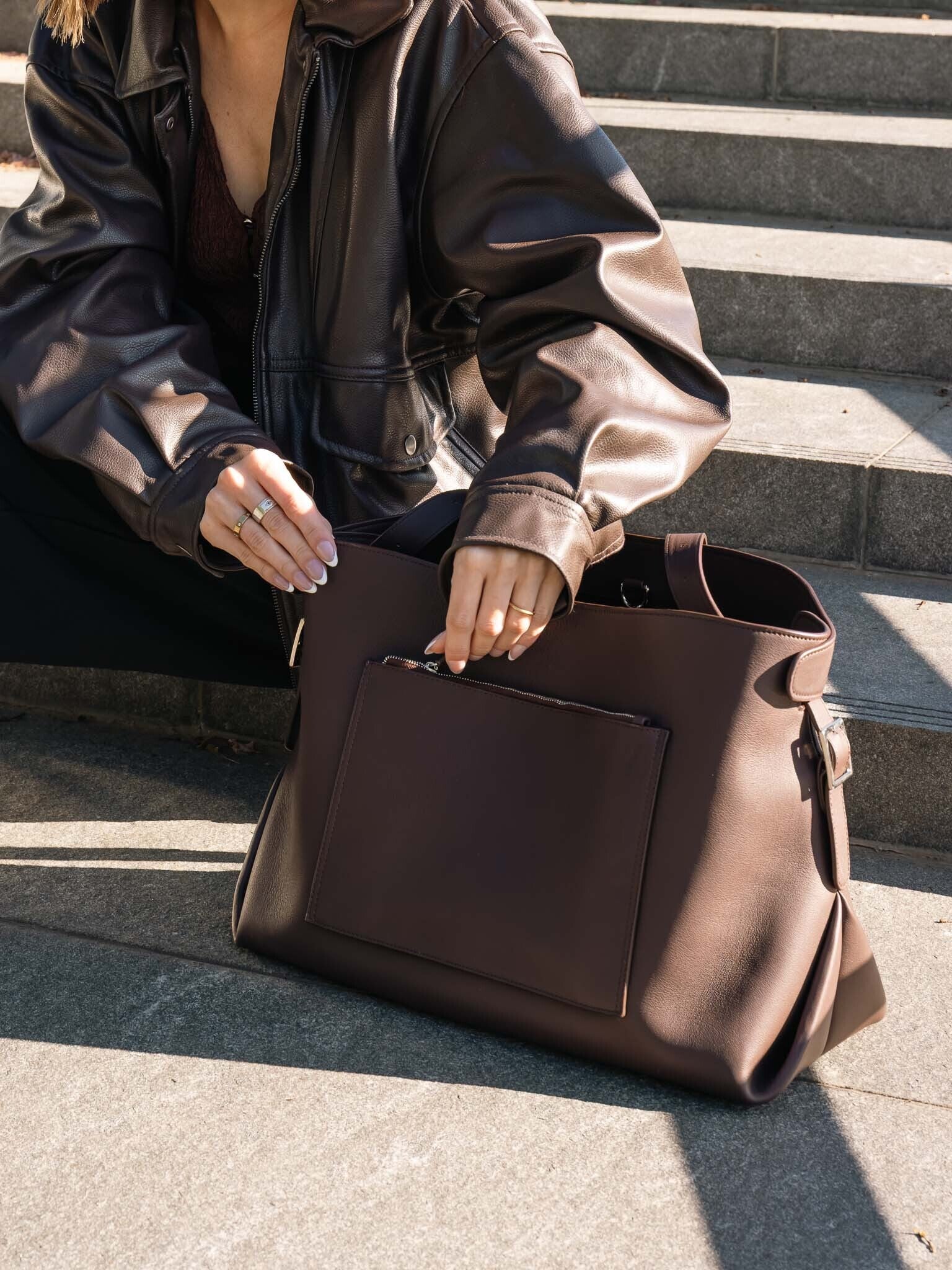 Woman unzipping the exterior pocket of the leather Metro Tote in a rich brown color.