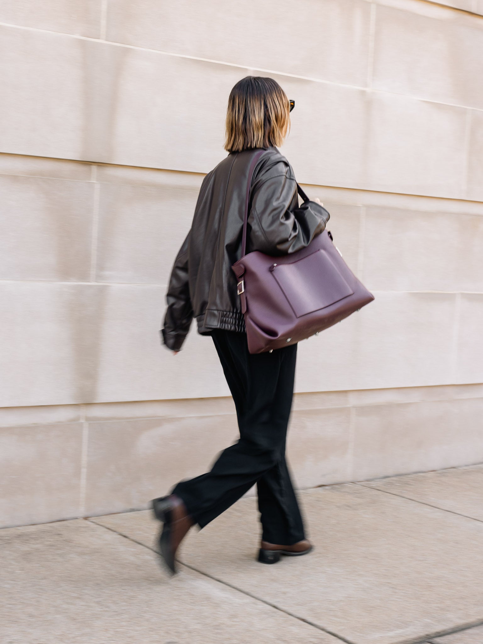 Woman walking with leather Metro Tote in a burgundy red on her shoulder.
