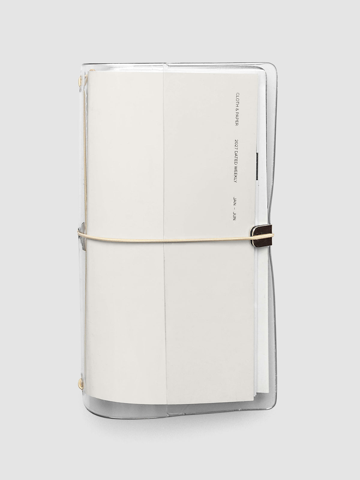 Closed clear vinyl travel notebook cover with a tan bungee cord and metal hardware, front page reading 2027 Dated Weekly January through June, A5 Slim size