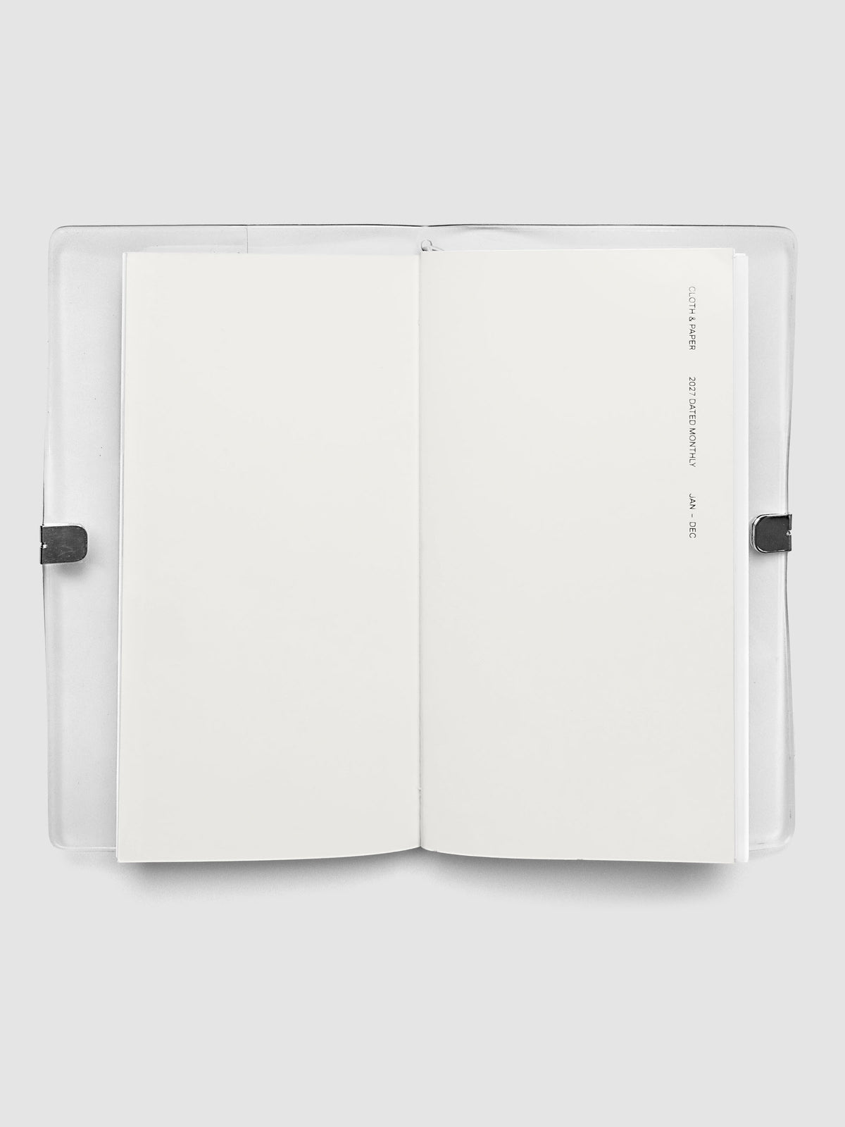 Open travel notebook showing a blank interior page, cover text reading 2027 Dated Monthly January through December, A5 Slim size
