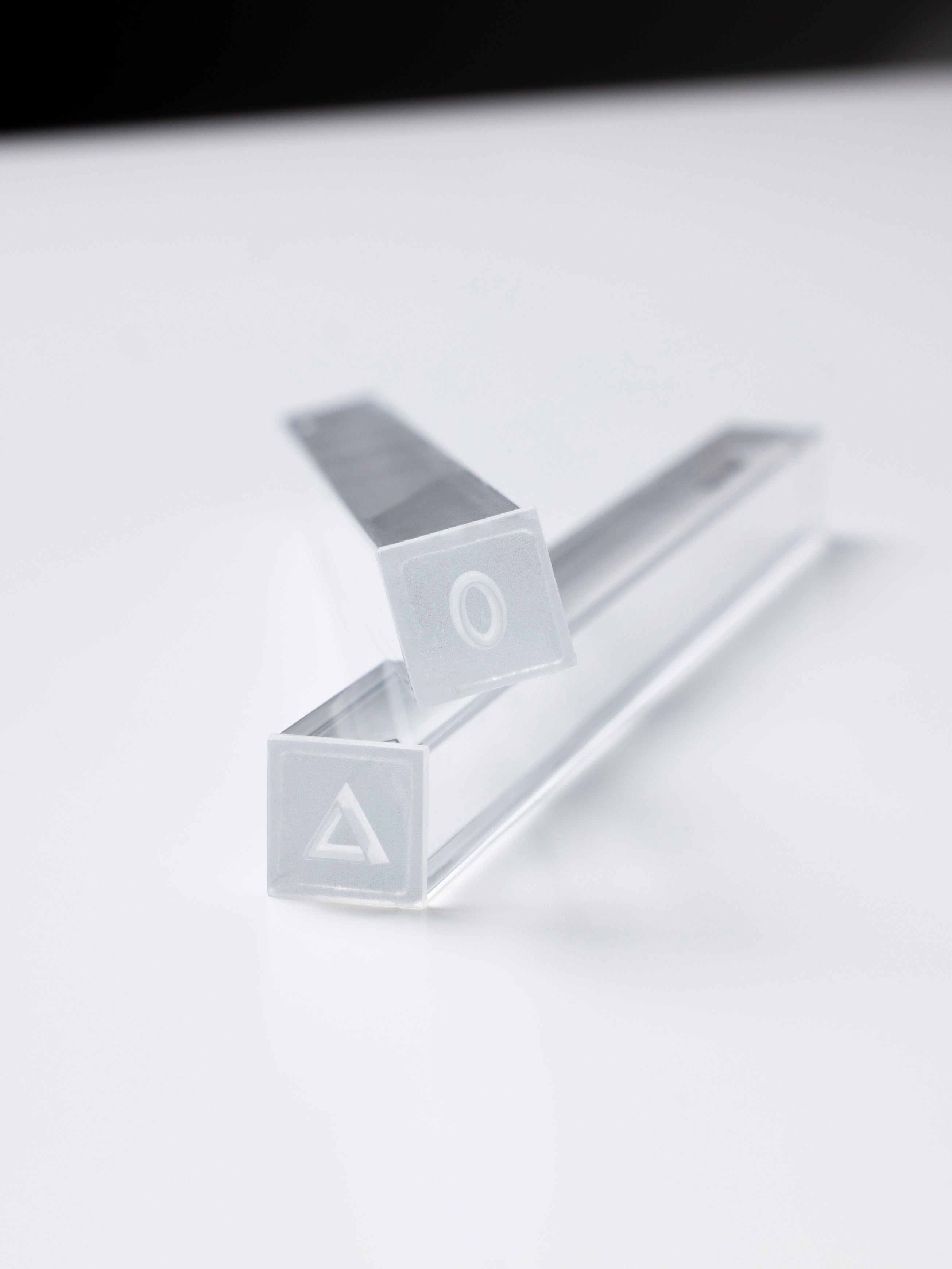 Two clear square pen cases with frosted end caps marked with a triangle and a circle, shown on a white surface