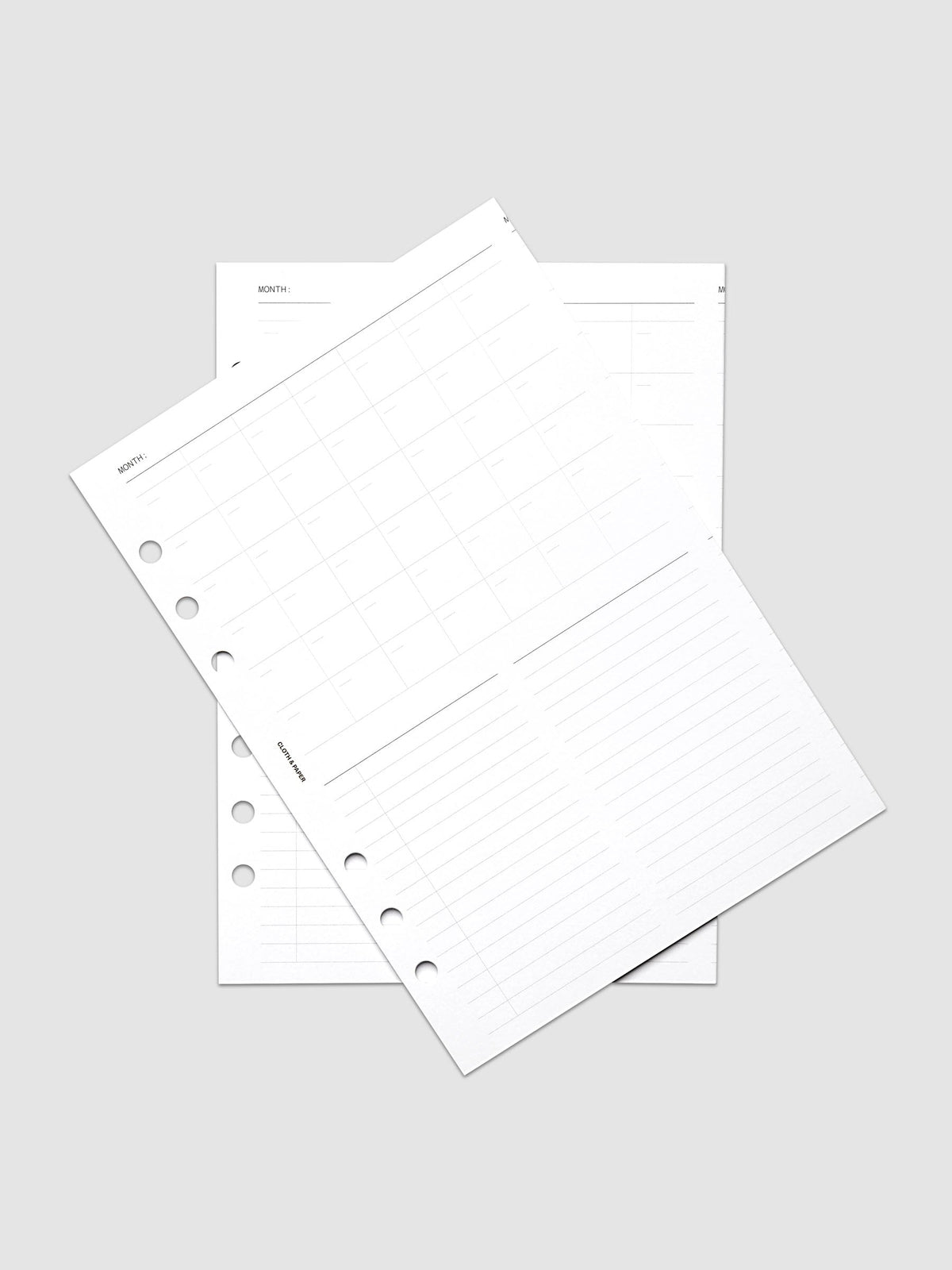 Monthly Fold Out Planner Insert Set of 2, A5 6-Ring Punch, both white inserts of the set overlapping at an angle on a pale gray surface, gray monthly grid and lined note columns visible on the top sheet