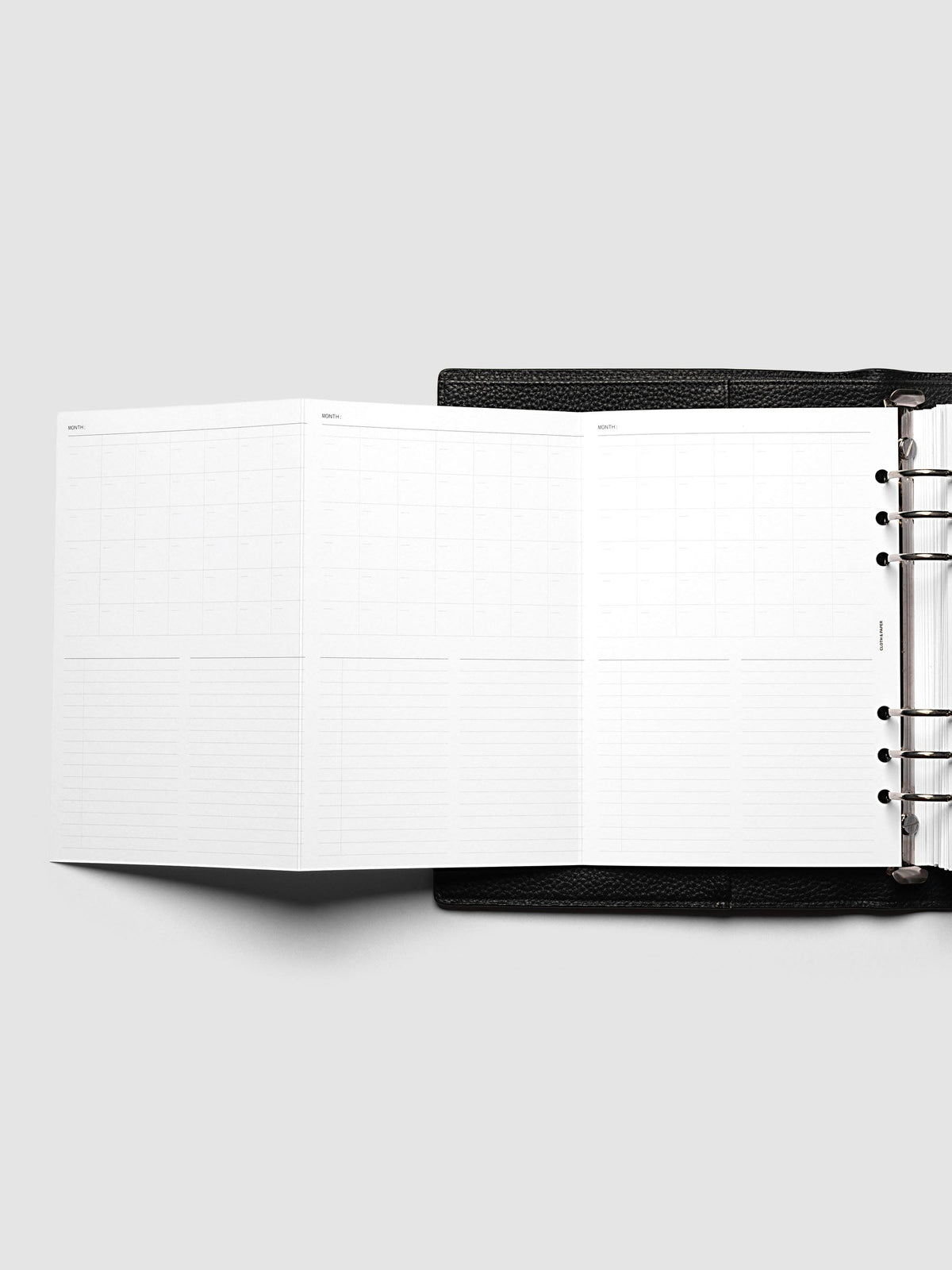 Monthly Fold Out Planner Insert Set of 2, A5 6-Ring Punch, the insert opened out to the left of a black leather ring bound planner, silver rings visible along the right edge of the frame