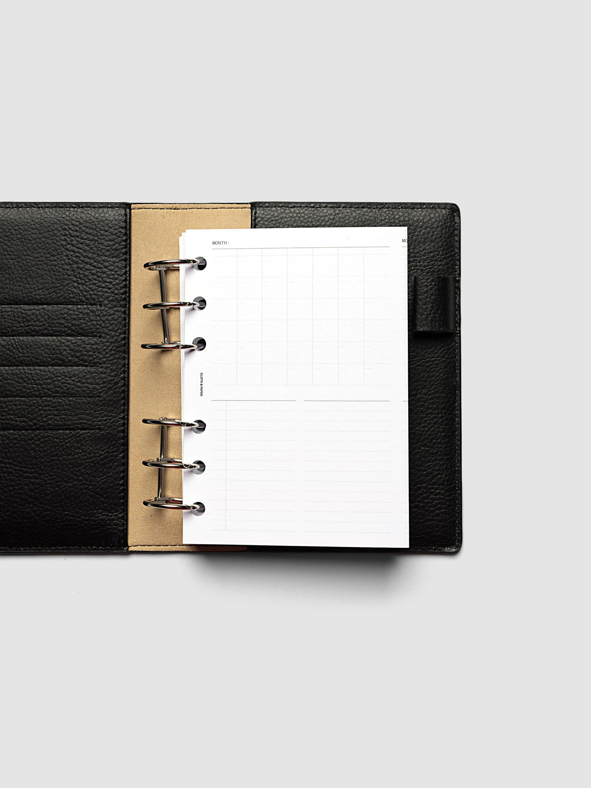 Monthly Fold Out Planner Insert Set of 2, A6 6-Ring Punch, the insert folded closed in a black pebbled leather ring bound planner with silver rings and a tan suede interior panel