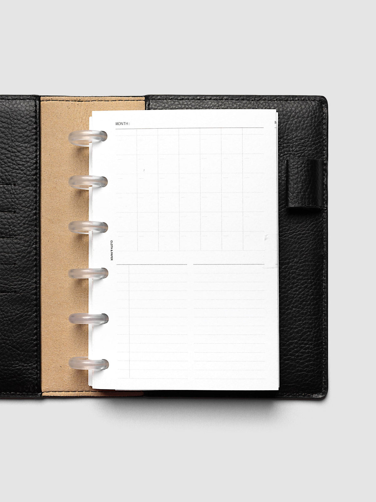 Monthly Fold Out Planner Insert Set of 2, CP Petite 6-Disc Punch, the blank insert folded closed in a black pebbled leather discbound planner with frosted clear discs and a tan interior panel