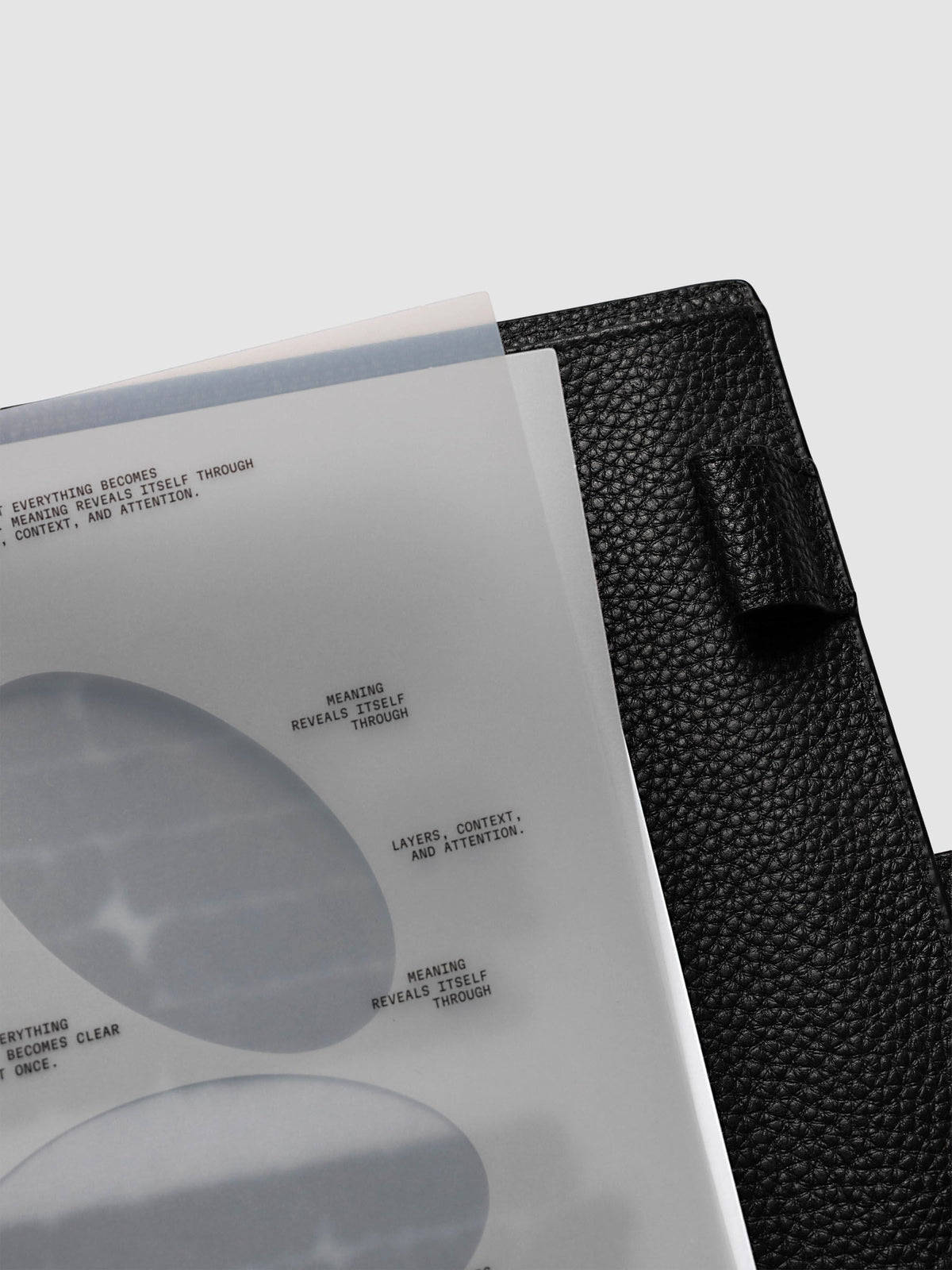 Nuanced Dashboard Trio, A5 6-Ring Punch, angled view of the top corner with two sheets lifted, black leather cover and pen loop at the right edge