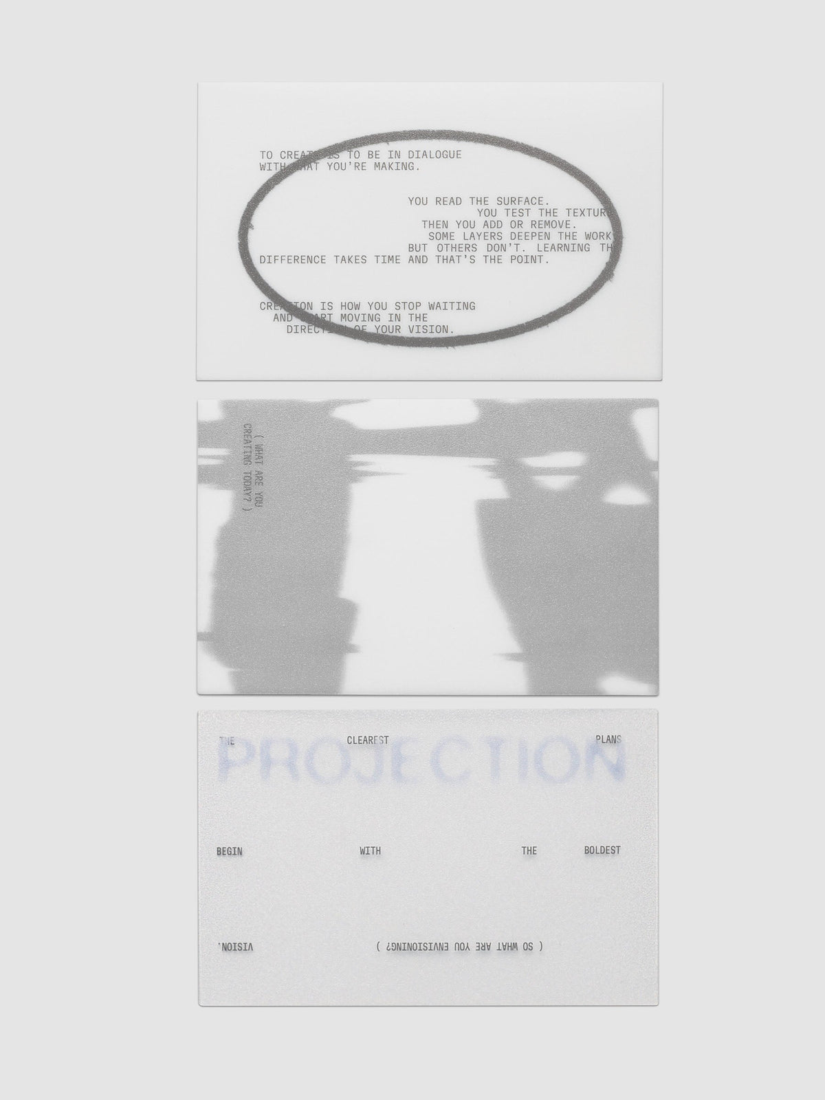Projection Journaling Card Set, three cards stacked in a column on a light gray background, one white with gray type inside a wide gray oval, one covered edge to edge in a blurred gray and white image, one pale gray with soft blue lettering behind scattered black type
