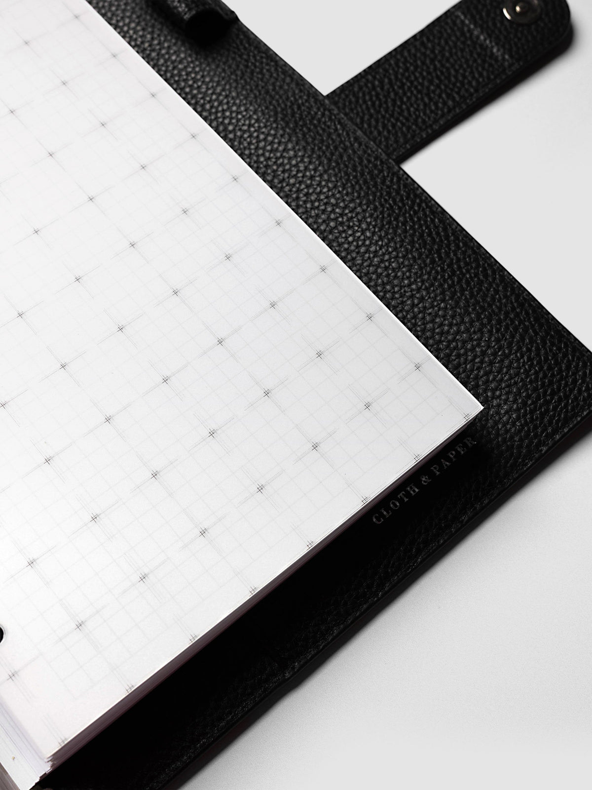 Grid Top Tab Dividers | Ultra-Thin, A5 6-Ring Punch, angled close-up of the outer edge of a divider resting on black pebbled leather, with the Cloth & Paper mark printed along the edge