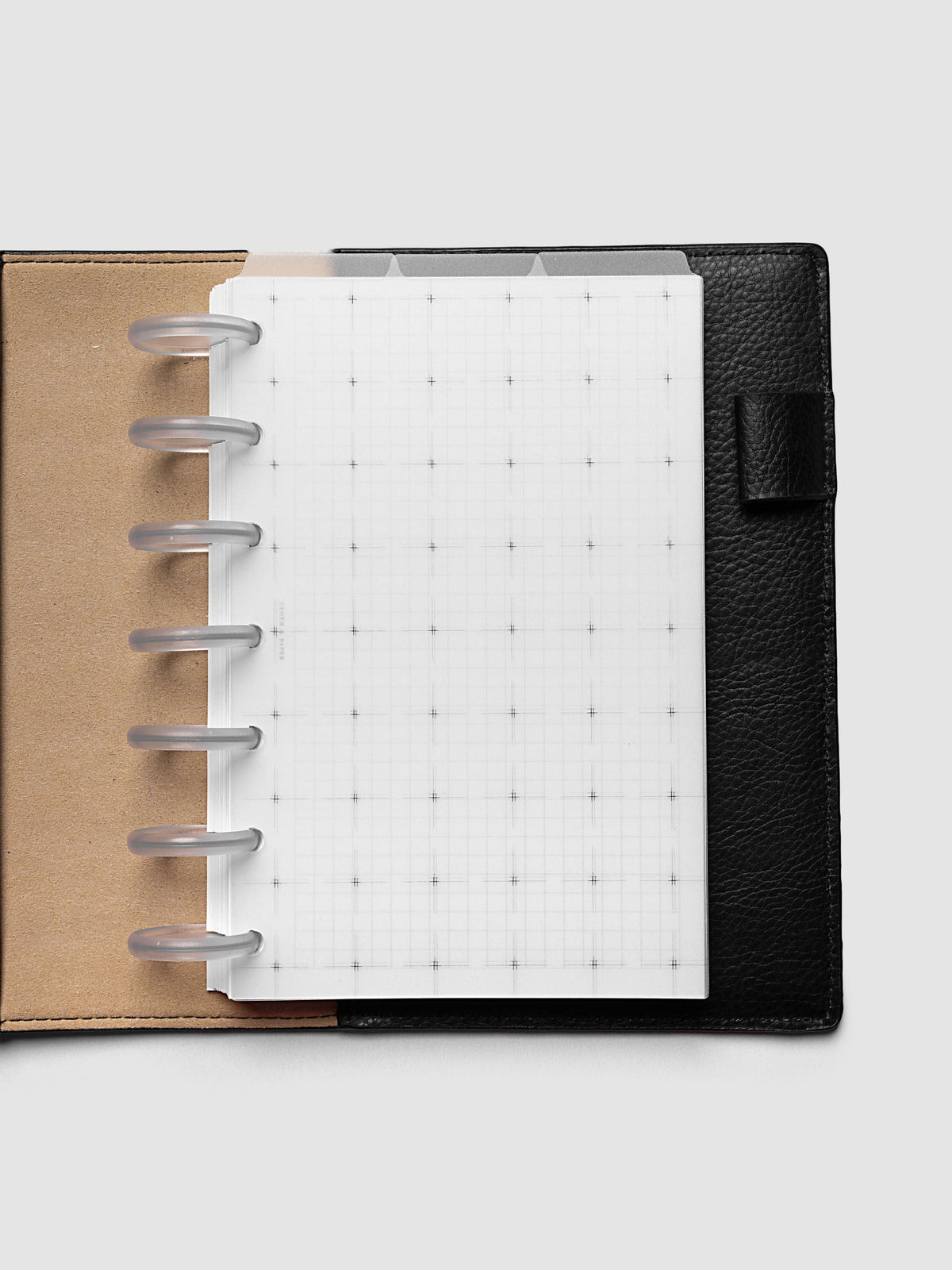 Grid Top Tab Dividers | Ultra-Thin, HP Mini 7-Disc Punch, dividers in an open black leather discbound planner with seven frosted clear discs and a tan interior, tabs staggered above a grid notes page