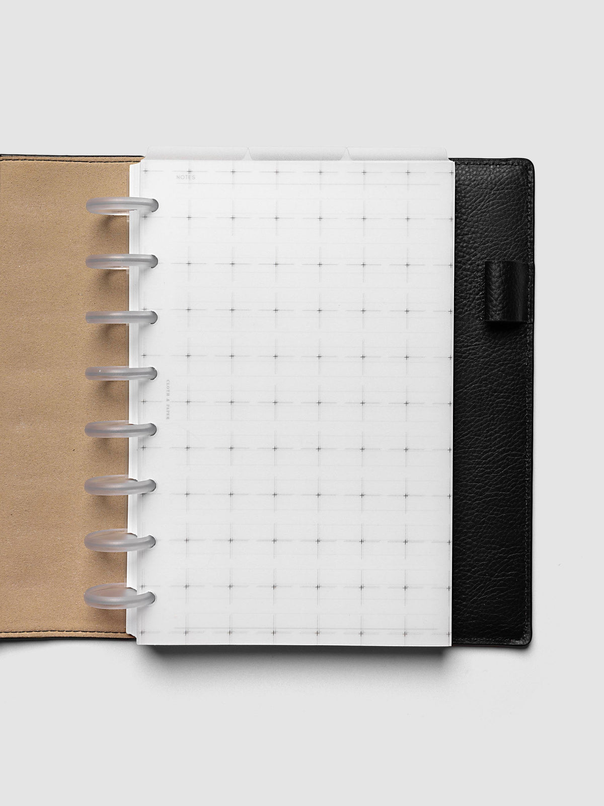 Grid Top Tab Dividers | Ultra-Thin, Half Letter 8-Disc Punch, dividers in an open black leather discbound planner with eight frosted clear discs and a tan interior, three tabs staggered above a grid notes page