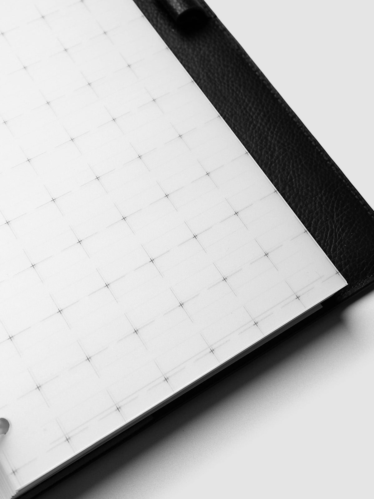Grid Top Tab Dividers | Ultra-Thin, Half Letter 8-Disc Punch, angled close-up of the grid printed divider lying across the black leather cover, showing the thin edge of the divider