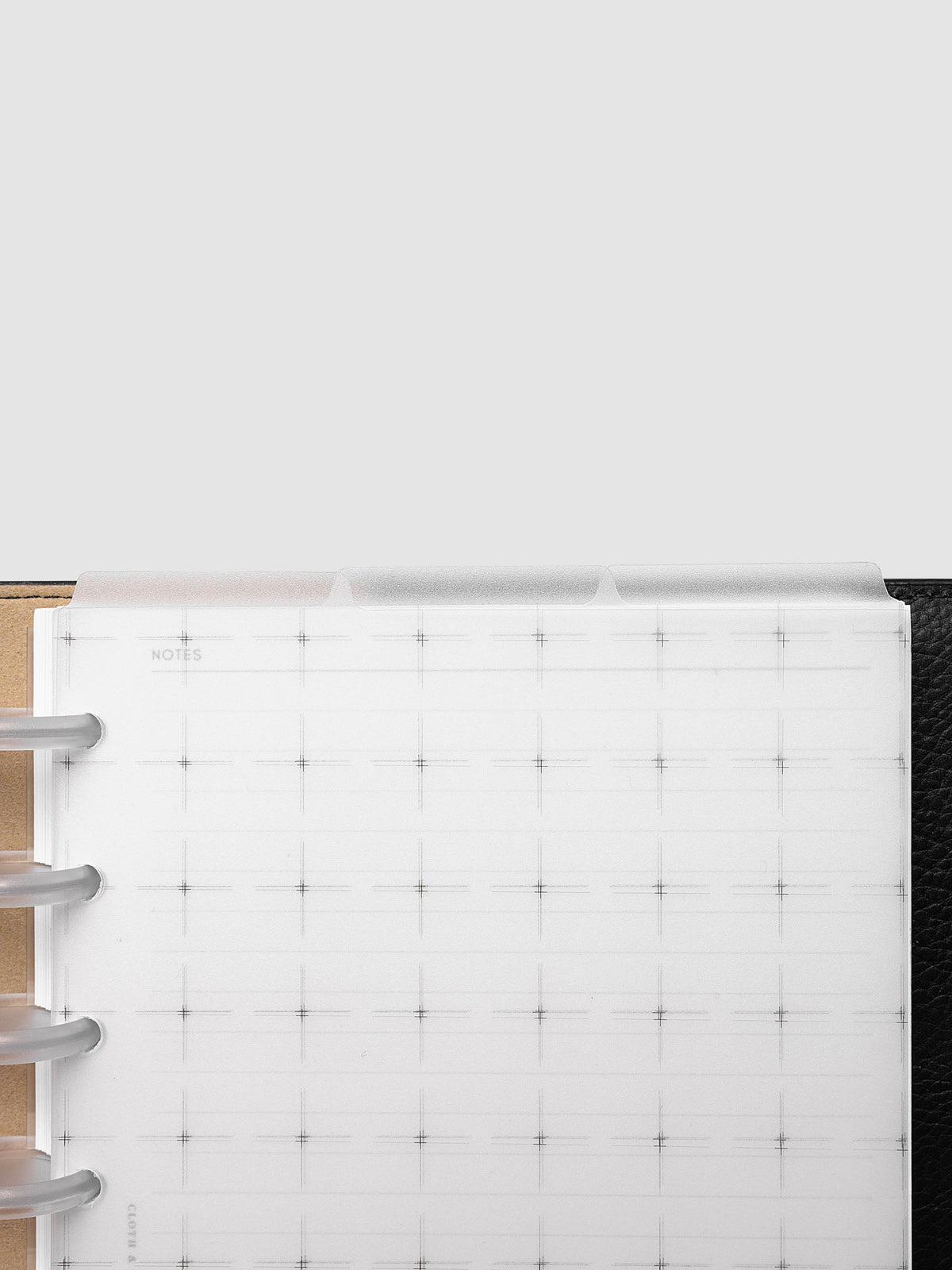 Grid Top Tab Dividers | Ultra-Thin, Half Letter 8-Disc Punch, cropped overhead view of the top edge in a discbound planner, three frosted tabs staggered above a grid notes page