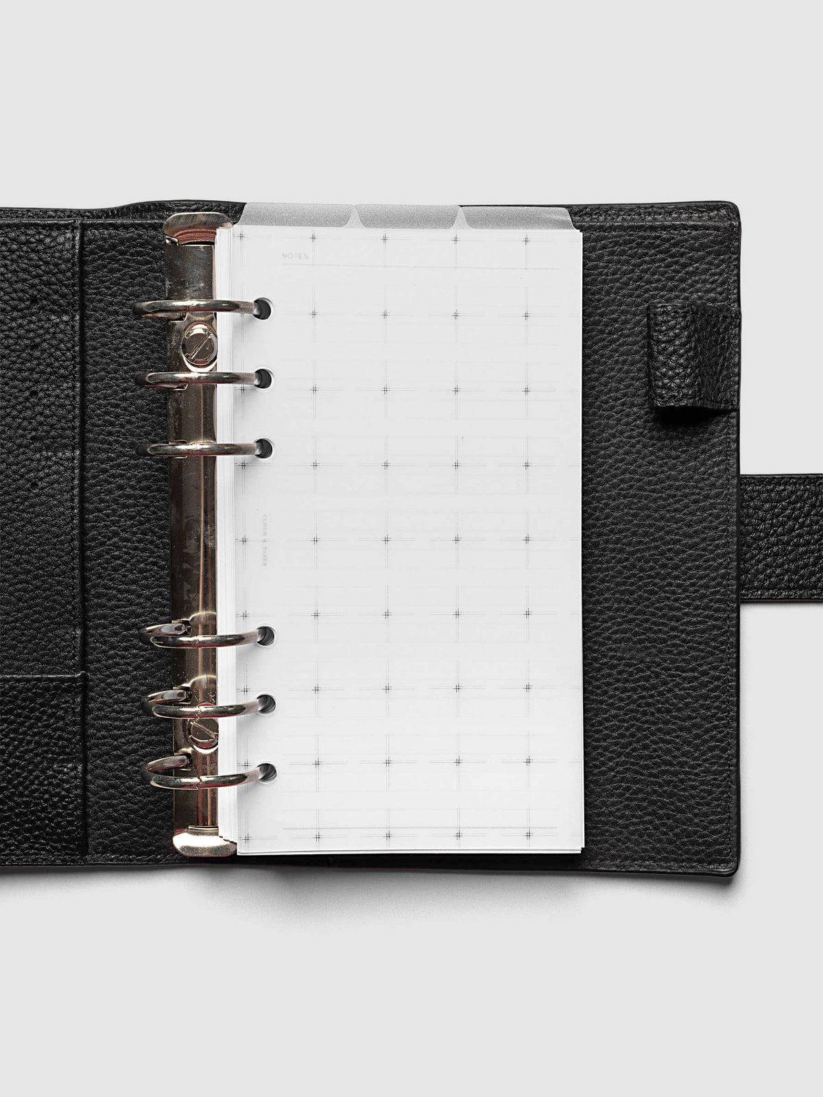 Grid Top Tab Dividers | Ultra-Thin, Personal 6-Ring Punch, dividers in an open black pebbled leather ring bound planner with silver rings, three tabs staggered above a grid notes page