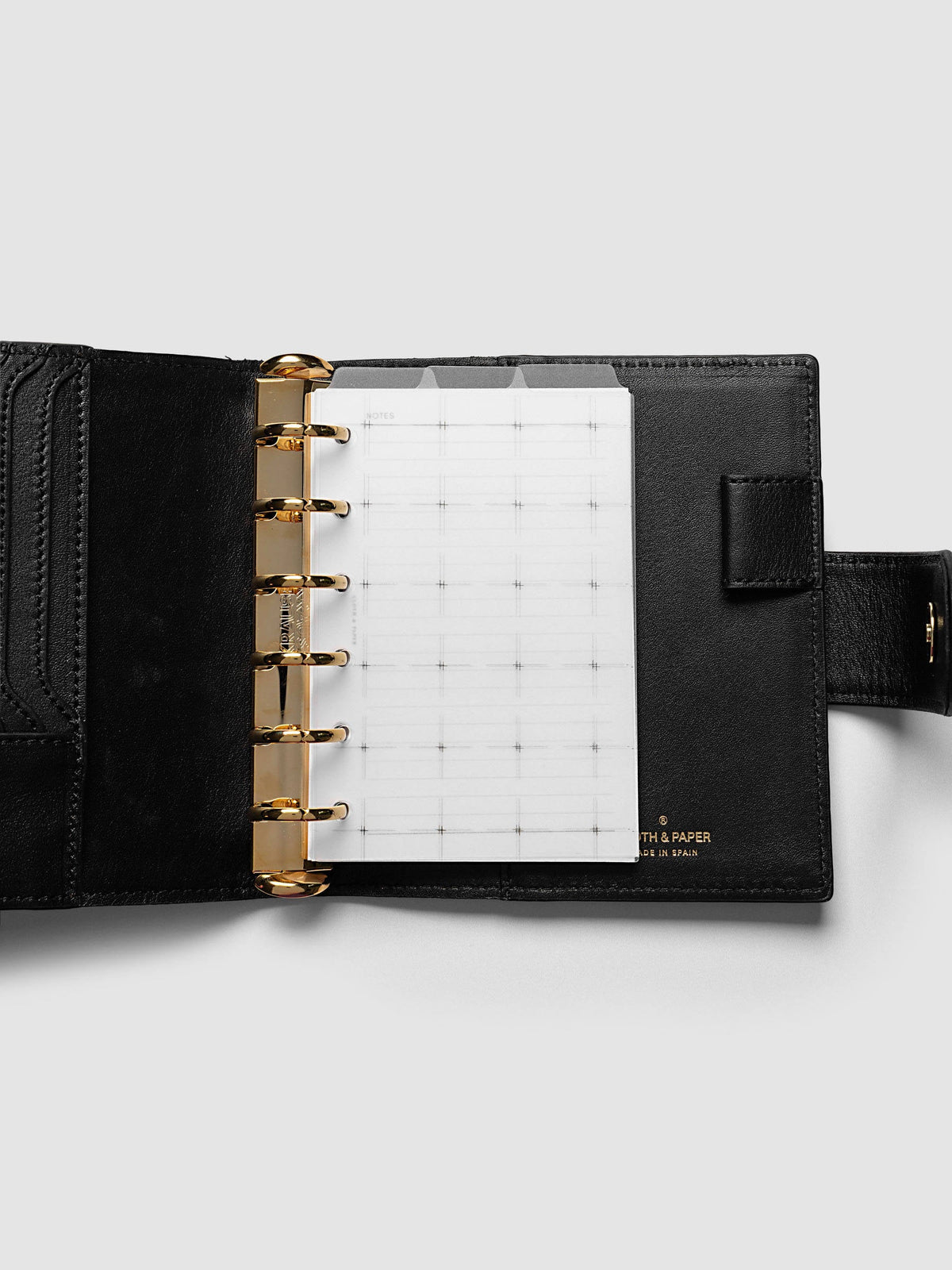 Grid Top Tab Dividers | Ultra-Thin, Pocket 6-Ring Punch, dividers in an open black leather ring bound planner with gold rings and card slots, three tabs staggered above a grid notes page
