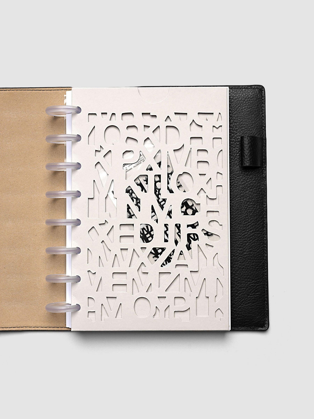 The Half Letter 8-Disc Punch Diecut Pocket Folder holding printed pages inside a black leather discbound planner, the contents showing through the cut letters