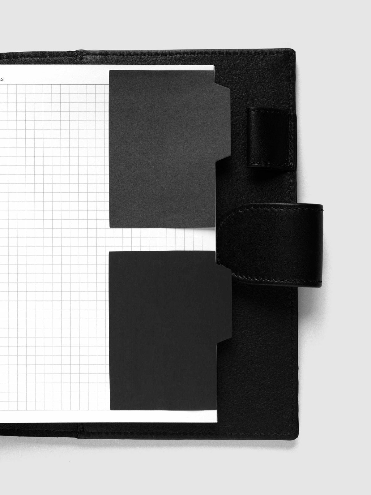 Blank Tab Sticky Note Set, Avant Garde, Cloth and Paper. One transparent and one matte note from the set placed on a grid insert in a black leather planner.
