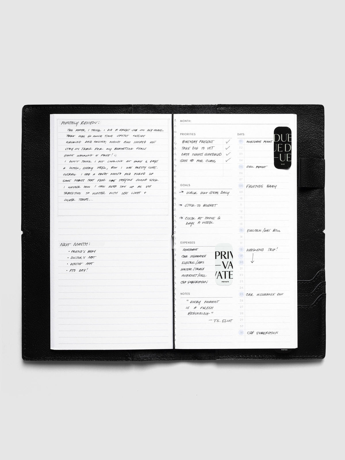 Monthly Overview A5 Slim inside a black travel notebook cover, filled in with a monthly review, priorities, goals, expenses and bills by day, with Private and Due stickers
