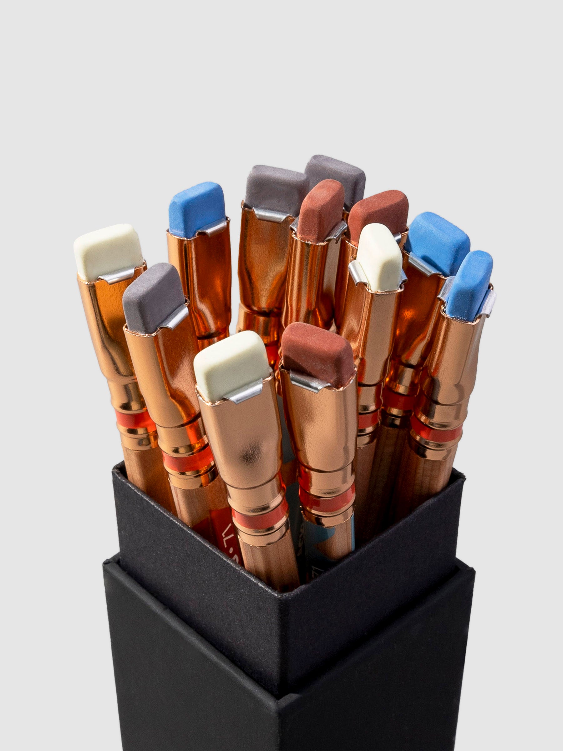 Closeup of pens, shown eraser-side up, on a neutral background. Erasers shown are blue, gray, brown, and white.