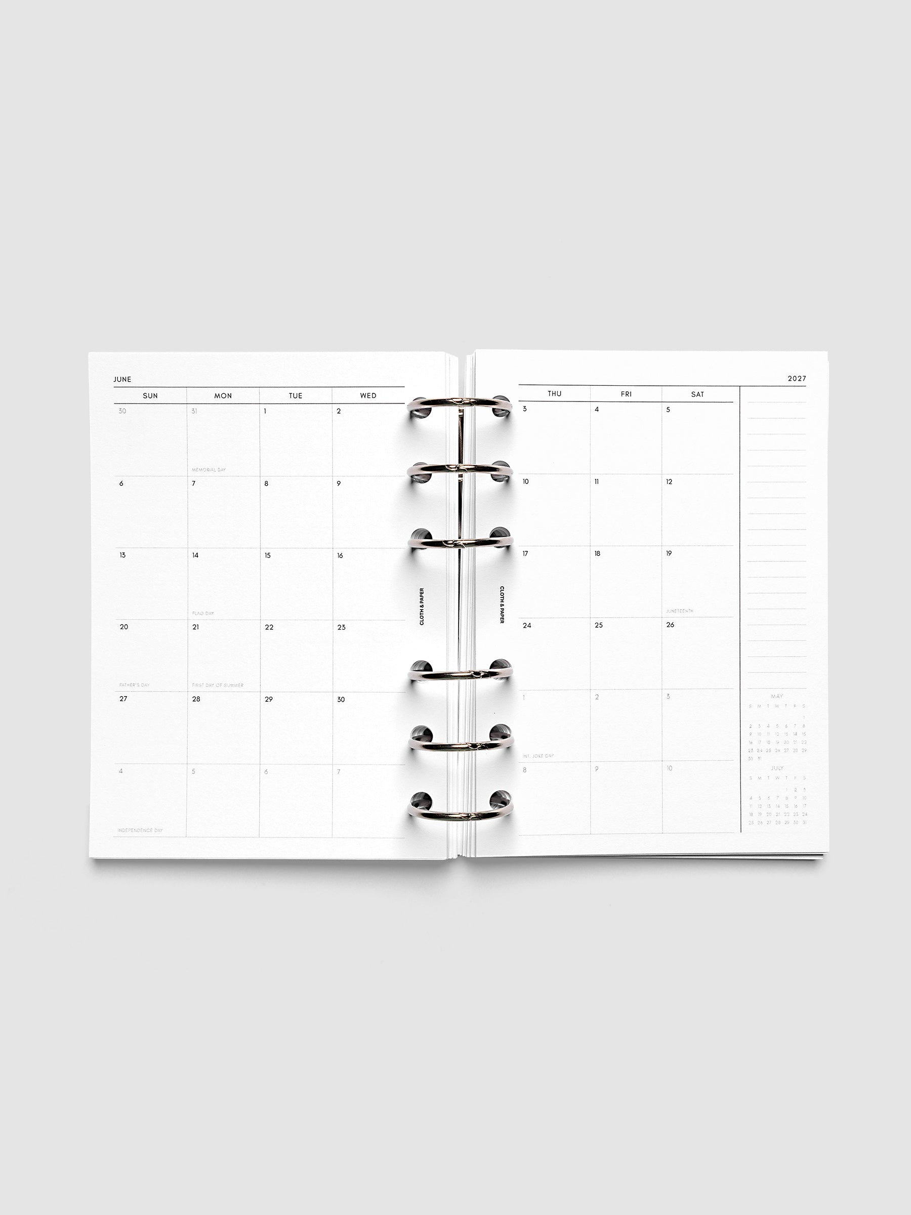 Open planner showing the full two-page 2027 Dated Monthly Sunday Start spread in A6 6-Ring Punch size, with calendar grid, notes column, and mini calendars in the bottom right corner