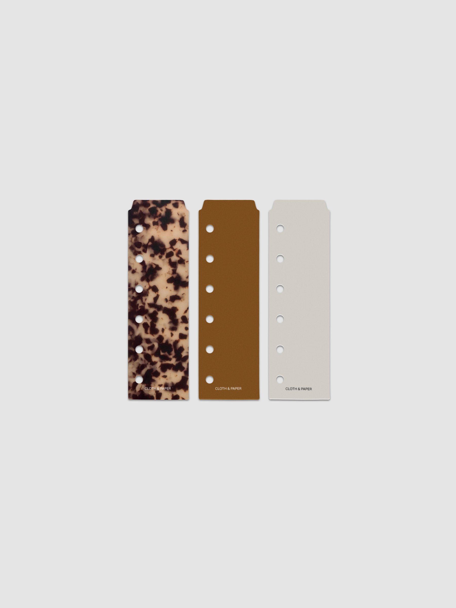 Narrow Page Marker Set Vol. 2, a set of 3 page markers for planners and notebooks shown in size Pocket. Includes one tortoiseshell pattern, one solid brown, and one solid grey page marker.