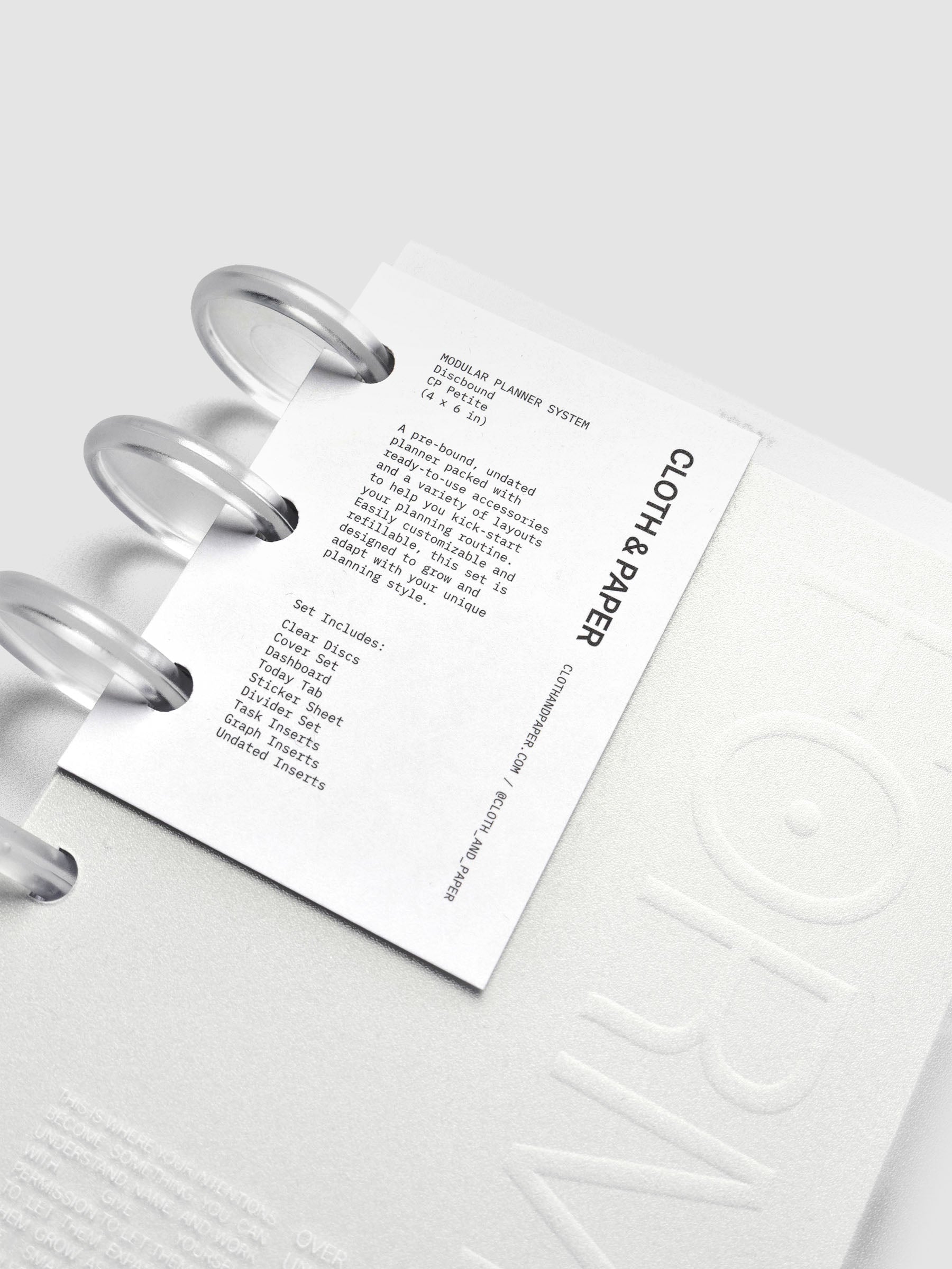 Close-up of a planner’s front tag label showing printed text describing an undated, customizable, refillable planner set with ready-to-use accessories and varied layouts.