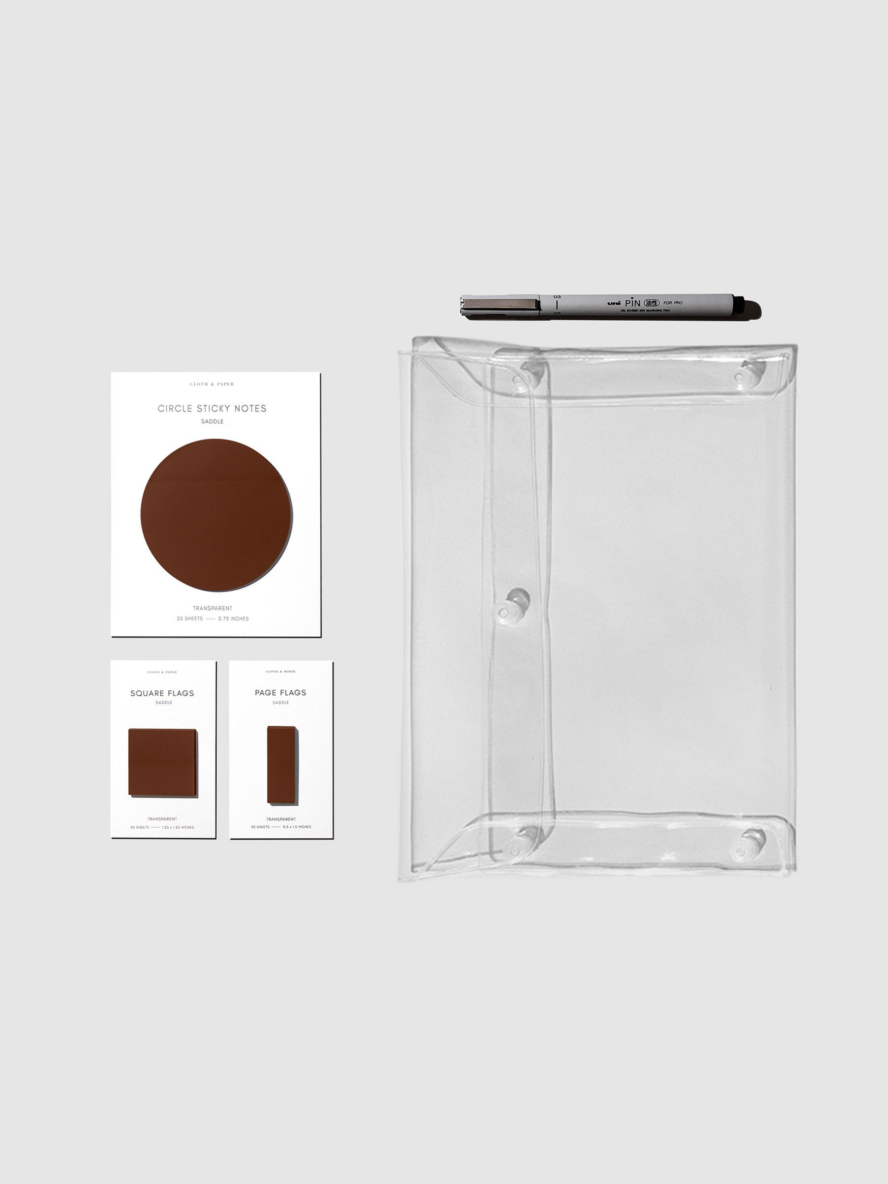 Matching set of circle sticky notes, page flags, and square page flags positioned next to a Uni Pin Marking Pen and Essentials Clear pouch. Sticky note color is Saddle.