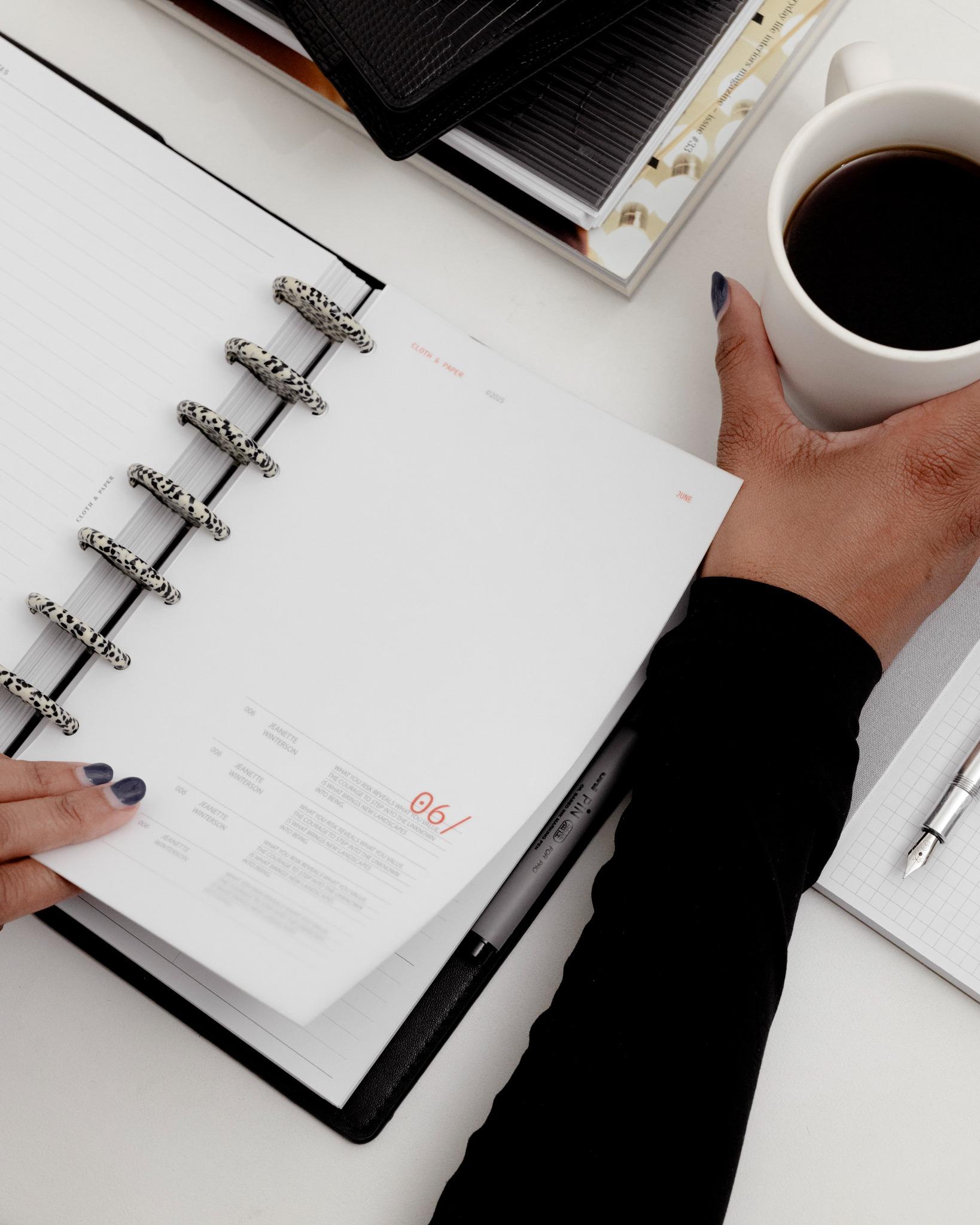 Top-down desk scene with a cup of coffee and the 2026 planner opened to June, accented with speckled discs