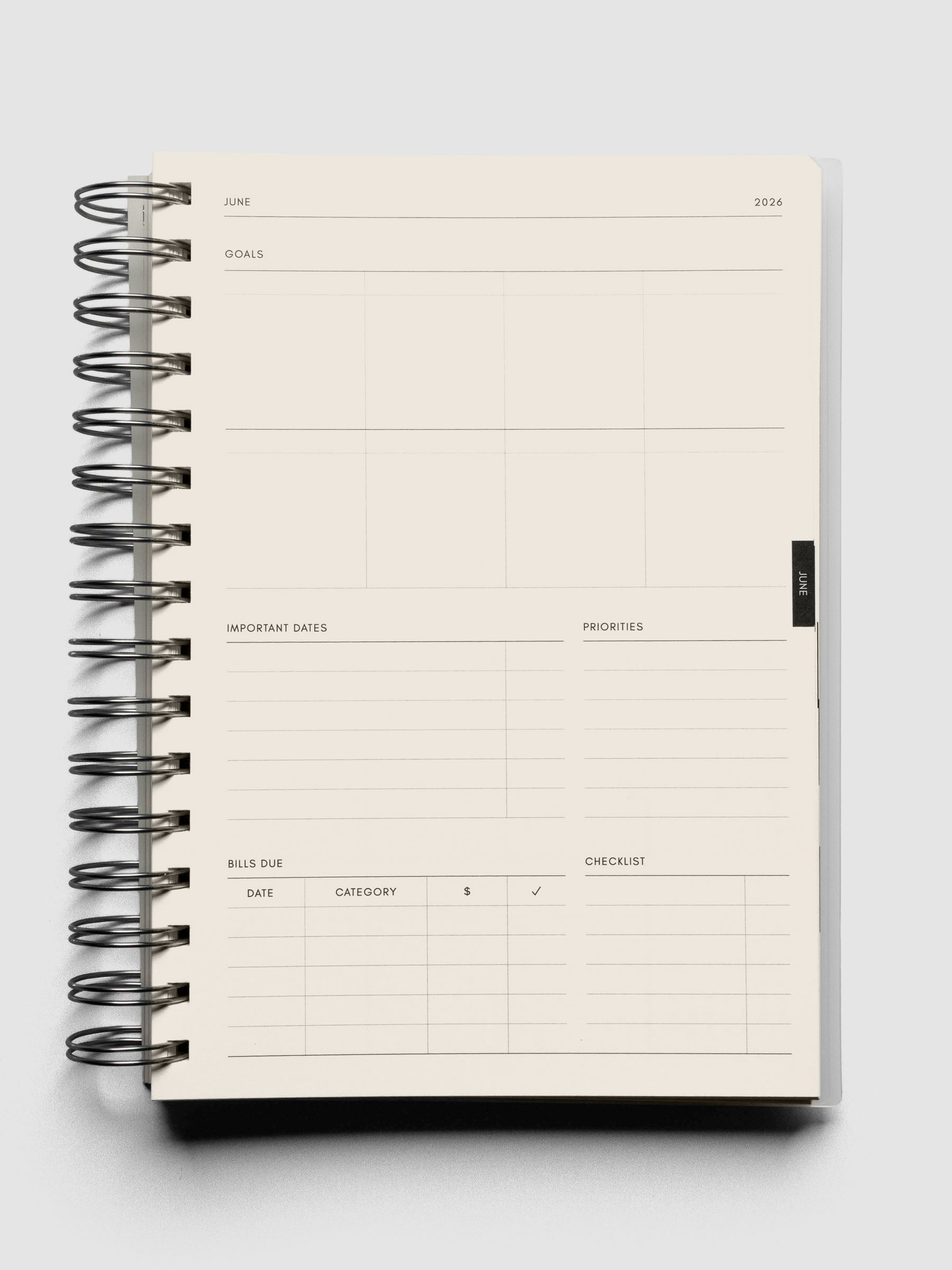 Open spiral notebook showing a monthly page with fields for goals, important dates, priorities, bills due, and checklists.