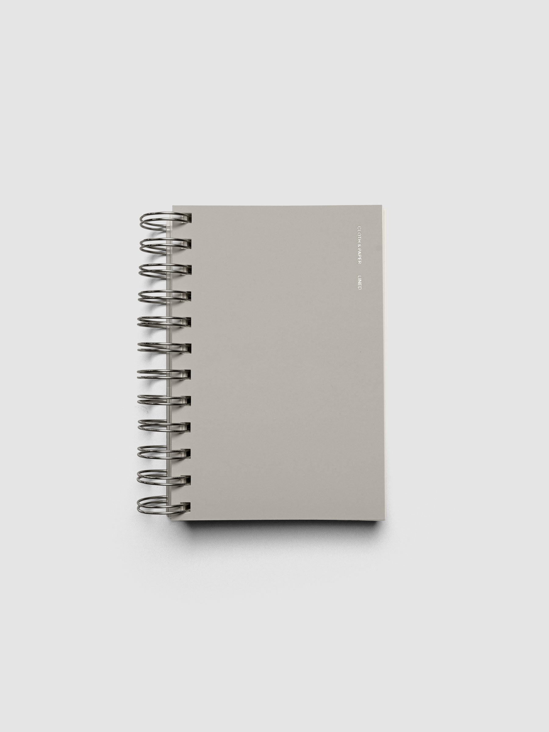 Spiral Notebook in size CP Petite and color Ash with Lined Notes interior pages shown closed displaying the soft touch dashboard.