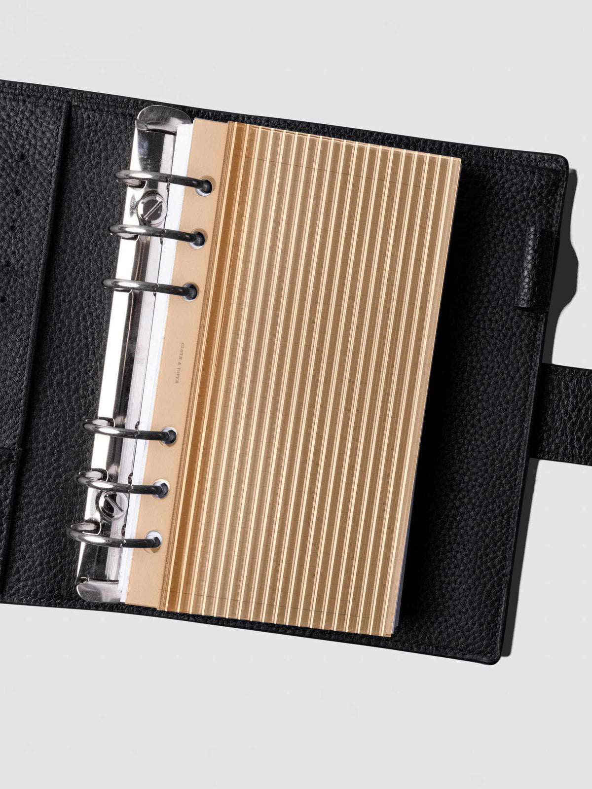 Bisque fluted planner dashboard in Personal size shown in a black leather six ring agenda with silver rings.
