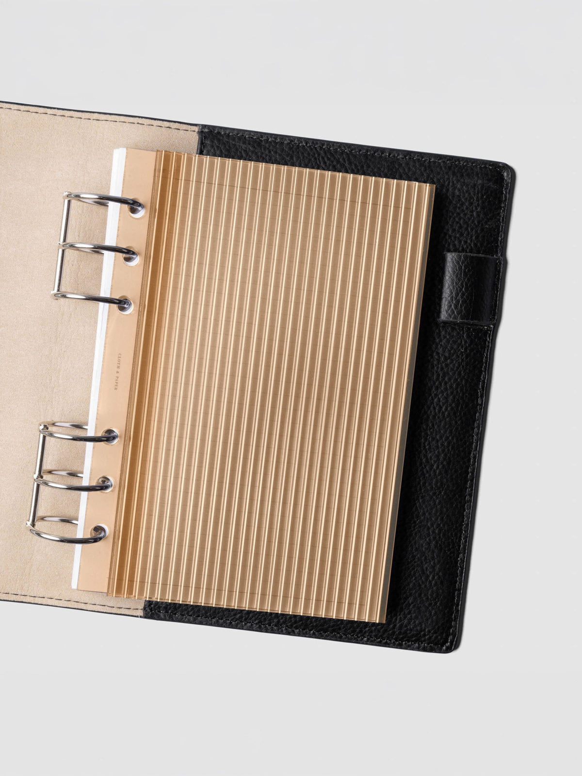 Bisque fluted planner dashboard in Personal Wide size shown in a black leather six ring agenda with silver rings.
