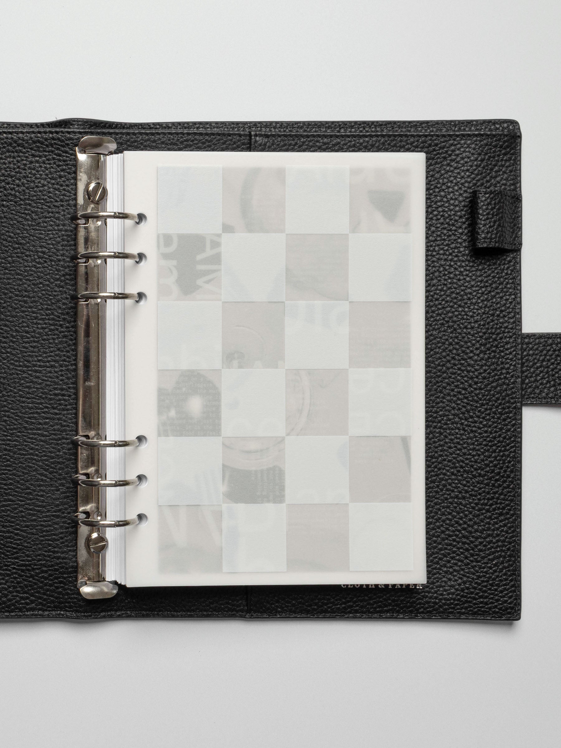 An A5 planner open to display the Ambiance Planner Dashboard trio layered together. The first translucent dashboard features a bold white checkered pattern overlay.