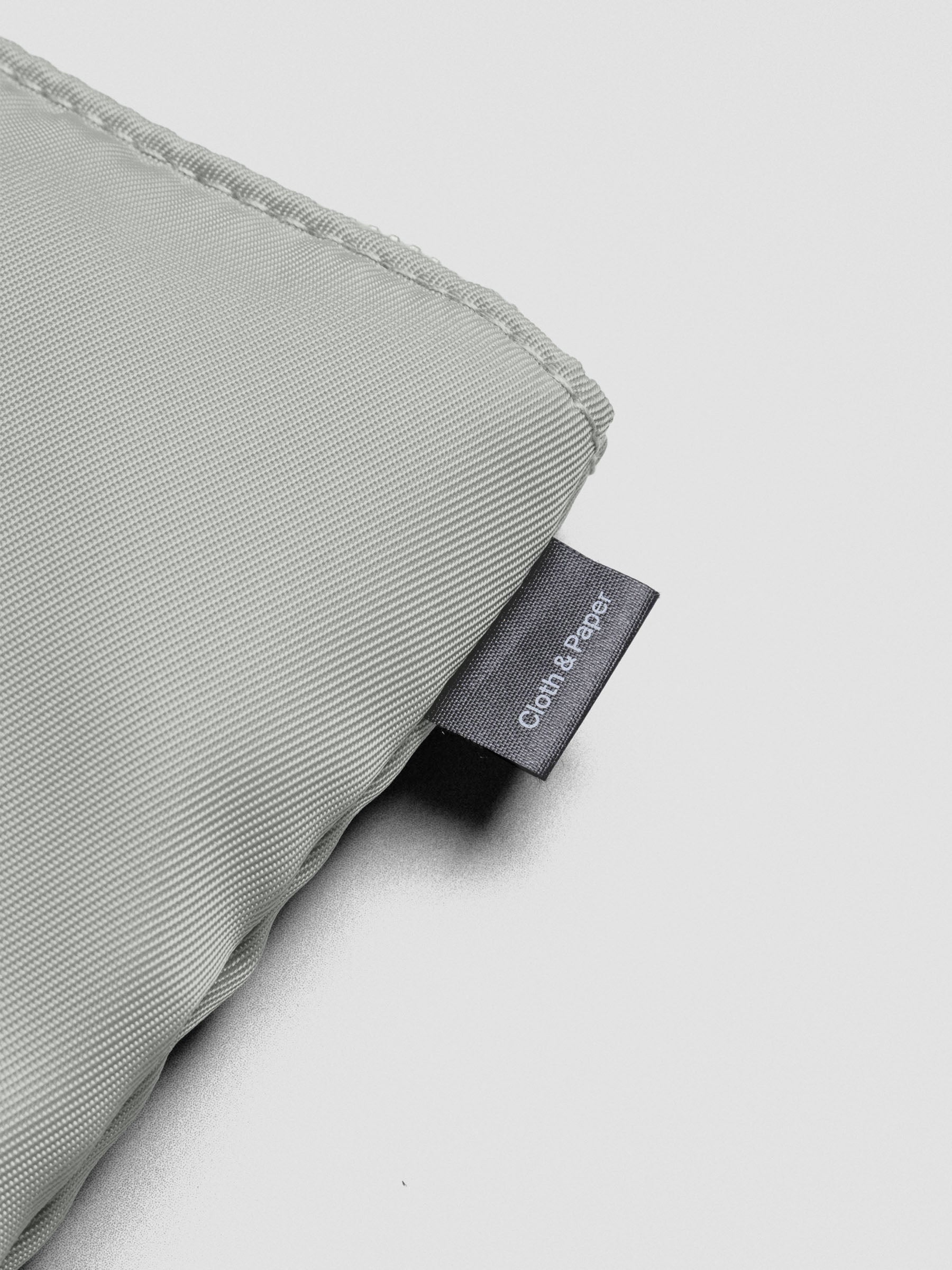 Close up of the stitching and tag on the green-grey nylon, padded bag reading "Cloth & Paper".