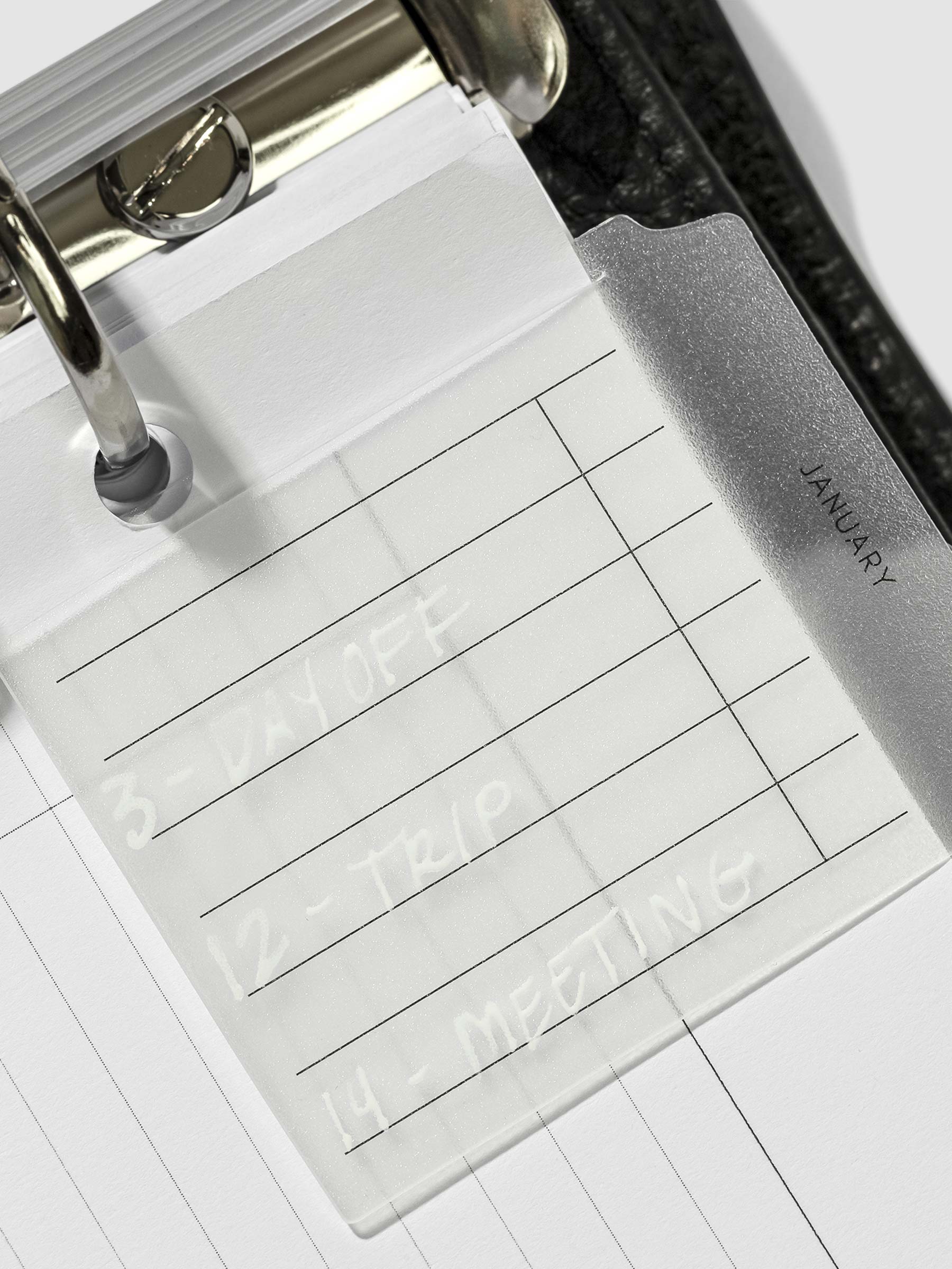 January Monthly Clear Index Tab in use inside a leather planner. It is written on with white paint marker.