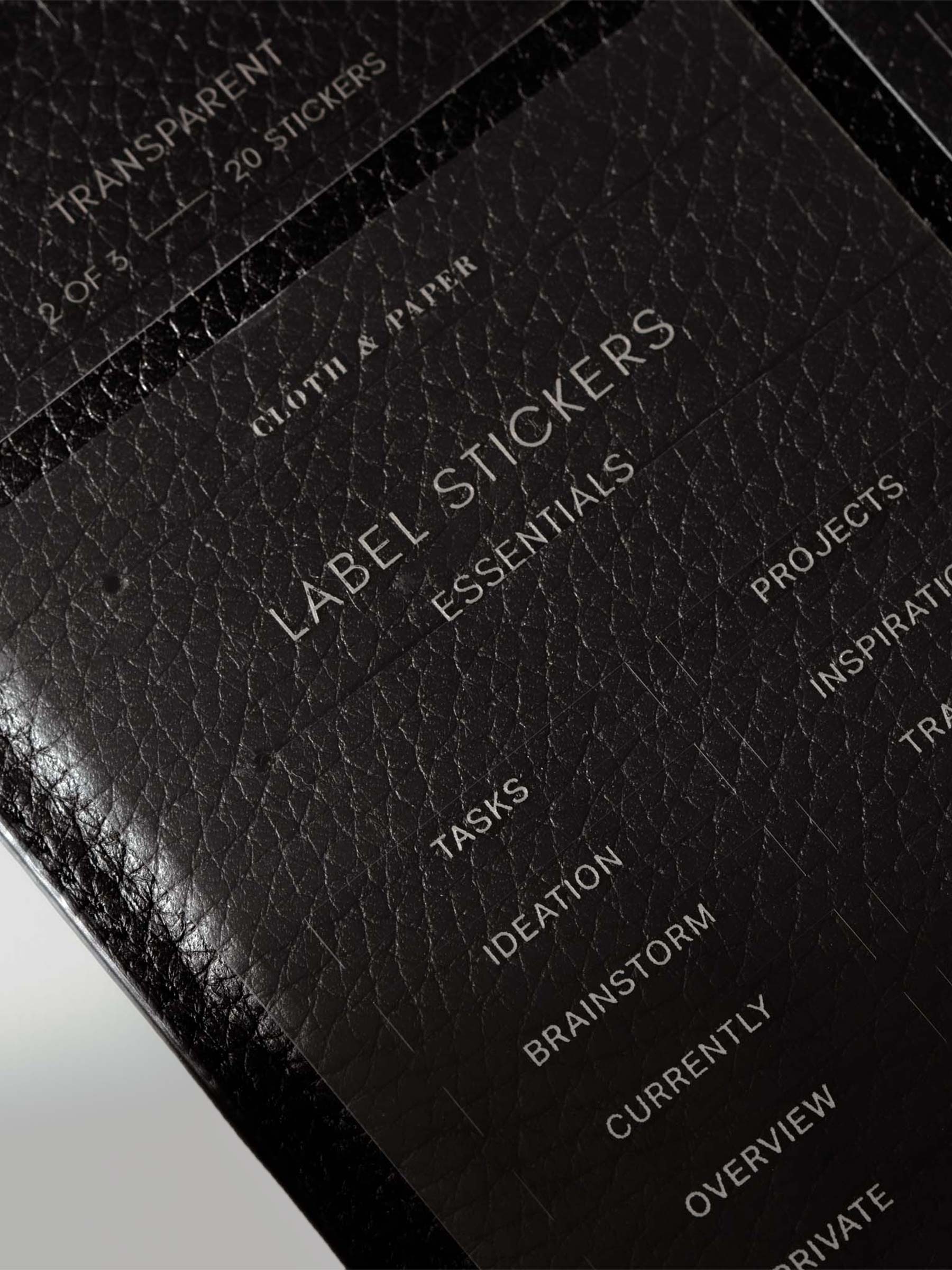 Close up image of the Clear Label Stickers against a black leather planner, which is titled to slight angle to the left