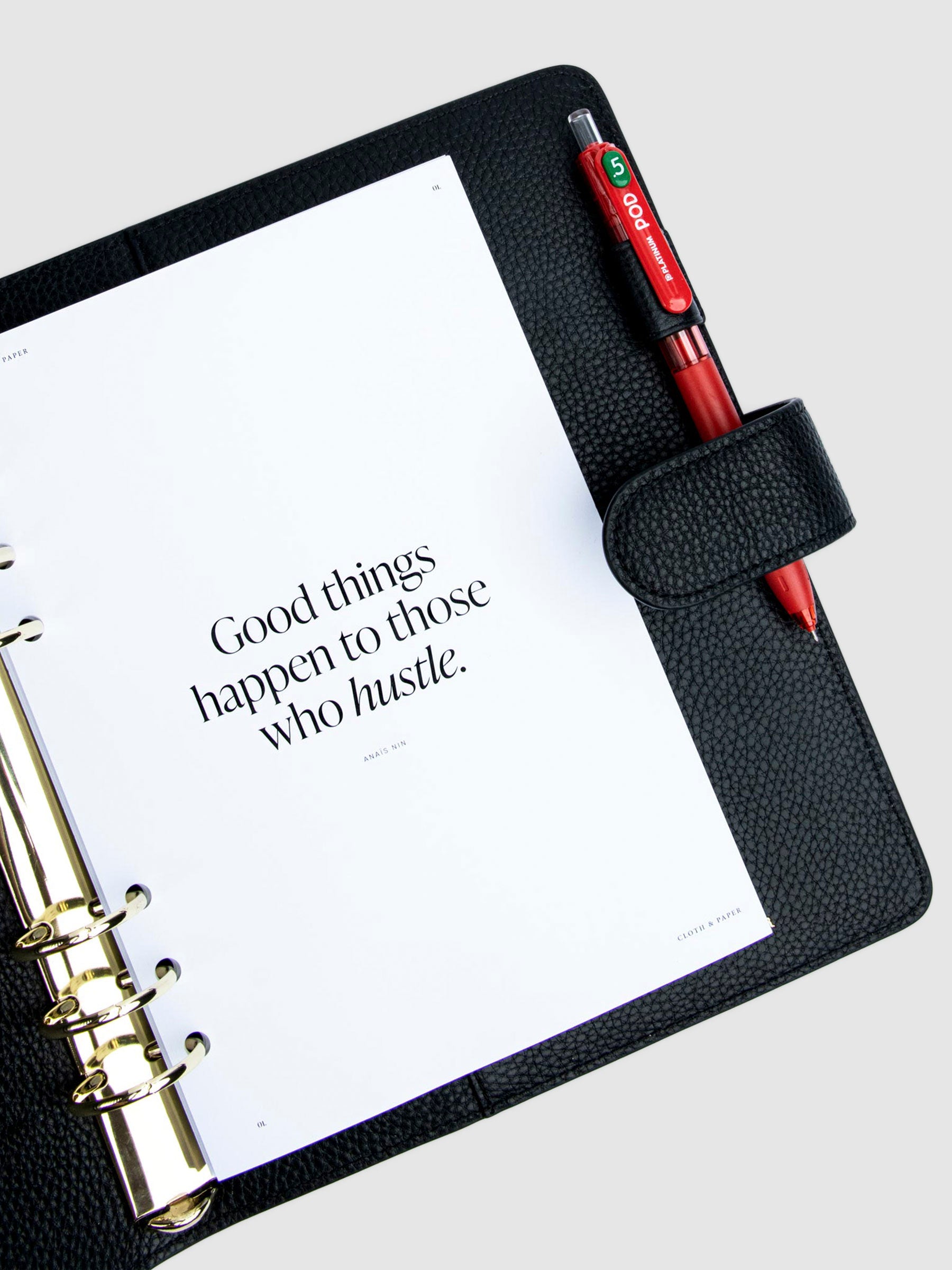 Creative Planning Insert Bundle, Cloth and Paper. Insert in use inside of a black leather agenda with gold rings on a neutral background. A red pen rests in the agenda's pen loop.