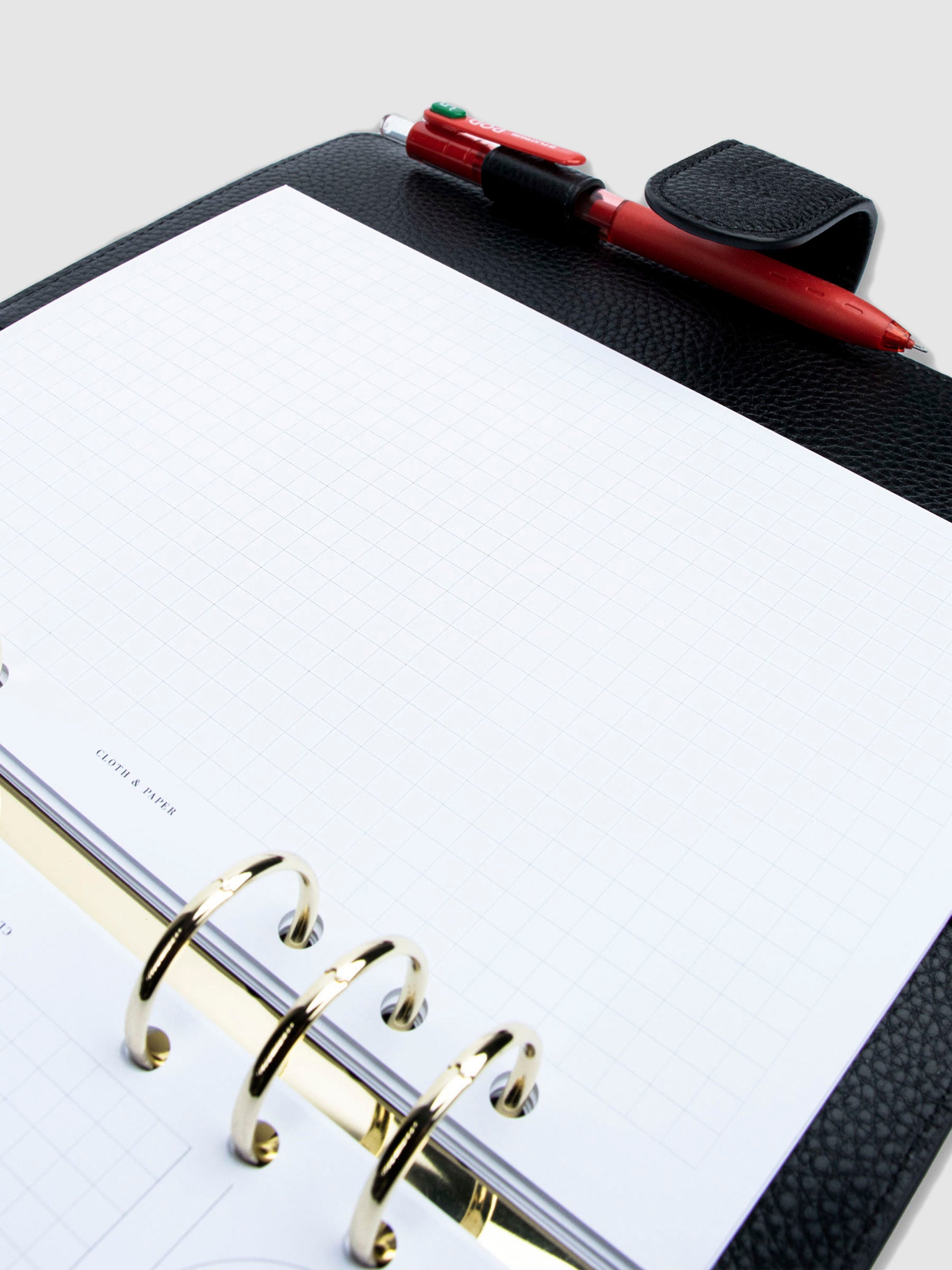 Creative Planning Insert Bundle, Cloth and Paper. Close up image of inserts in use inside a black leather agenda with gold rings. A pen rests in the agenda's pen loop. Pictured insert page shows graph notes.