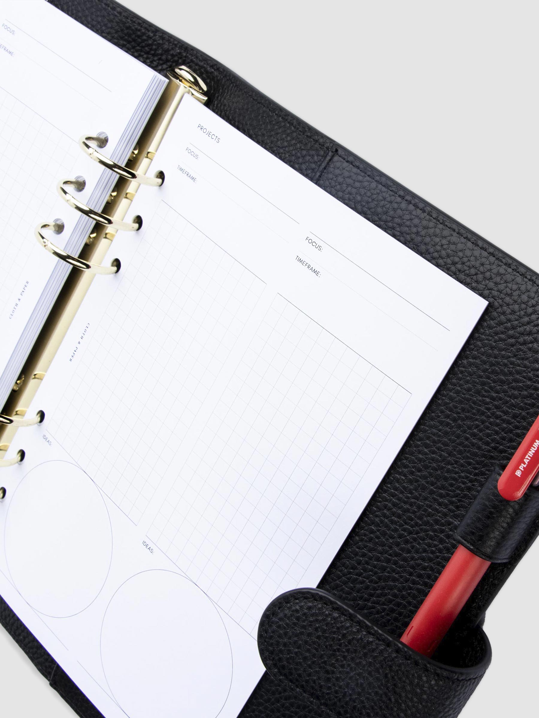 Creative Planning Insert Bundle, Cloth and Paper. Inserts in use inside a black leather agenda with gold rings. A red pen rests in the agenda's pen loop. Inserts shown are two Project pages.
