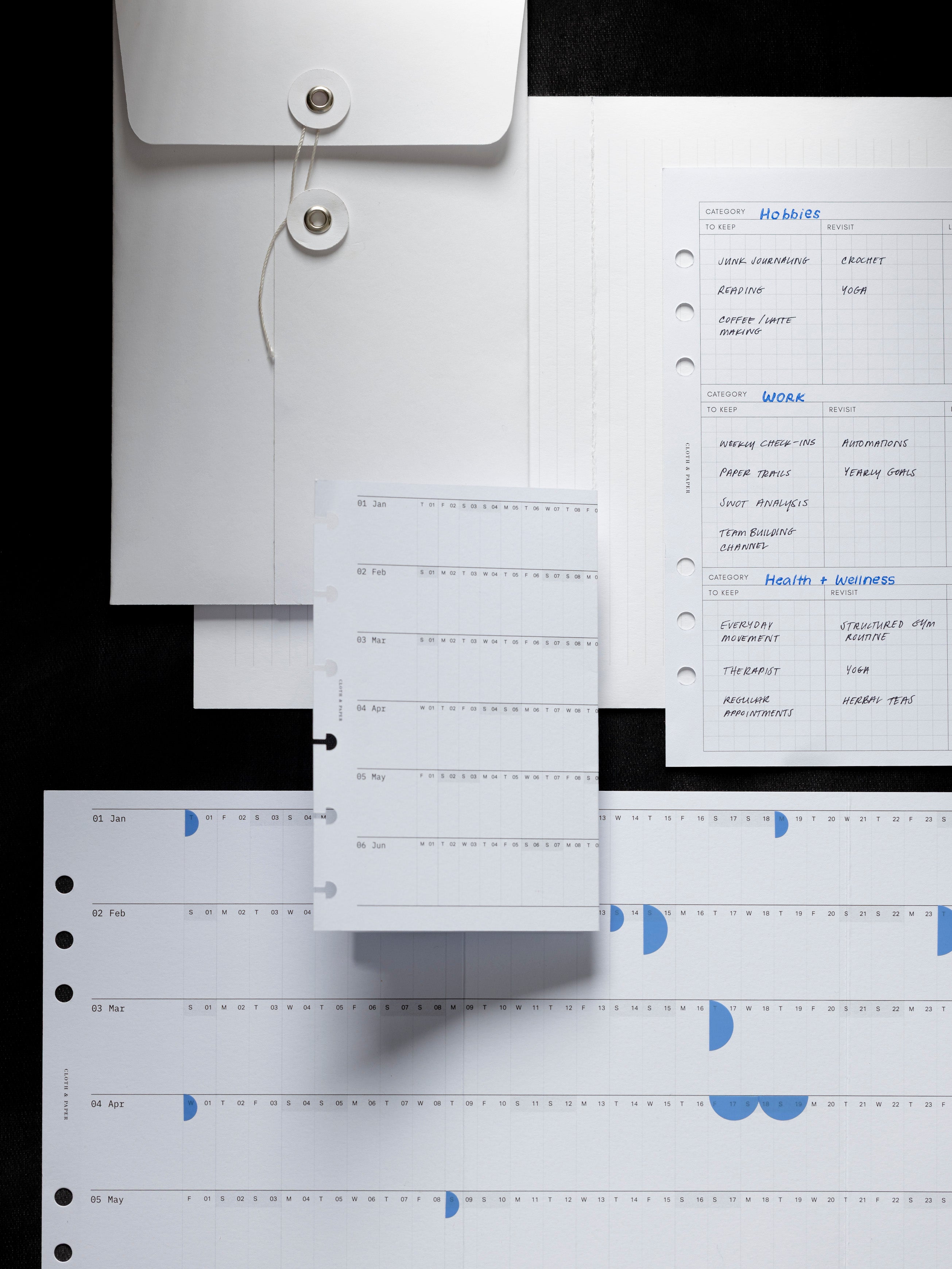 Envelope, planner inserts, and fold out calendar with handwritten notes on a dark background.