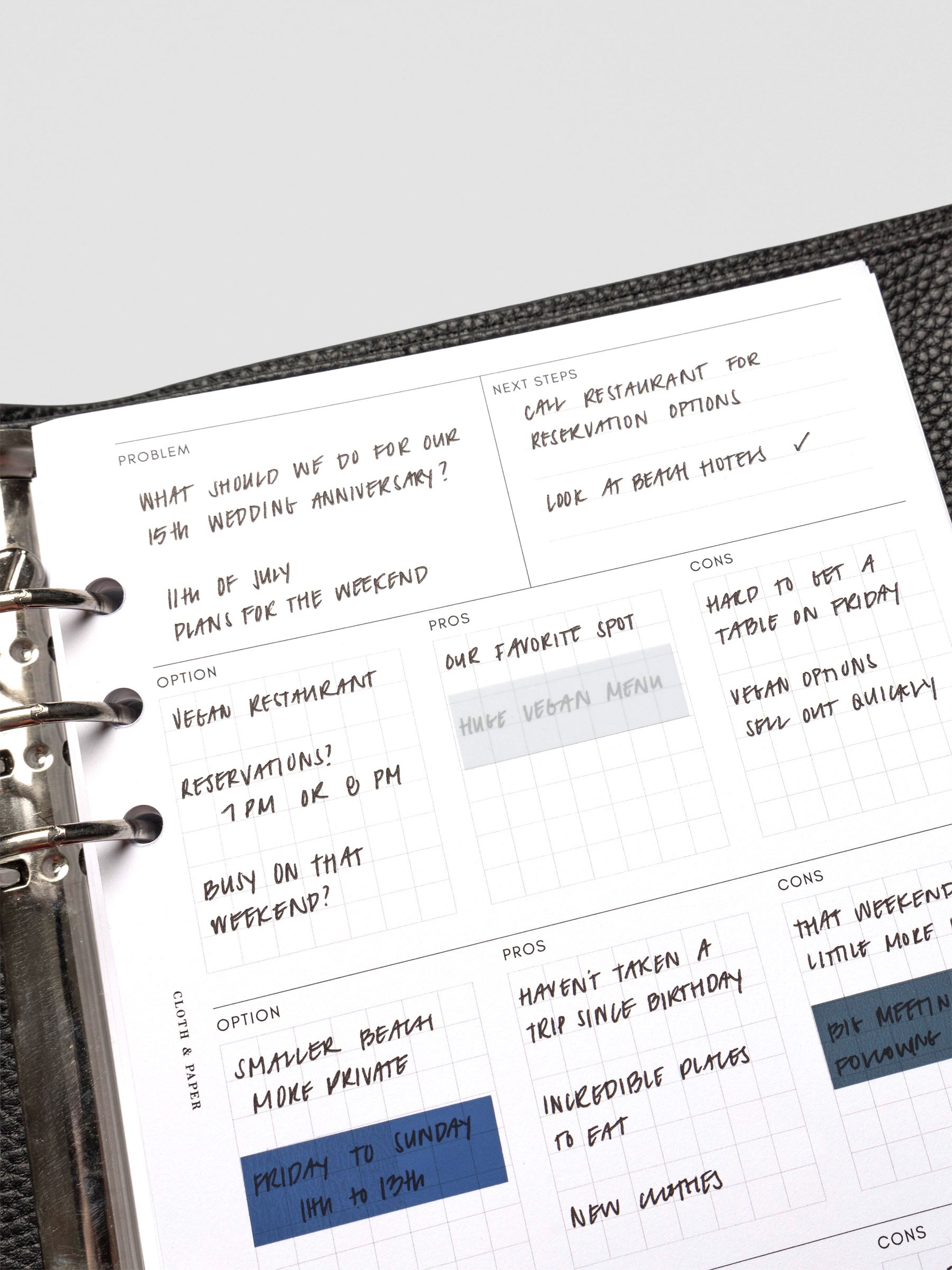 An A5 decision-making insert filled with handwritten notes, outlining a problem, next steps, and options with pros and cons. The page is secured in a black leather planner.