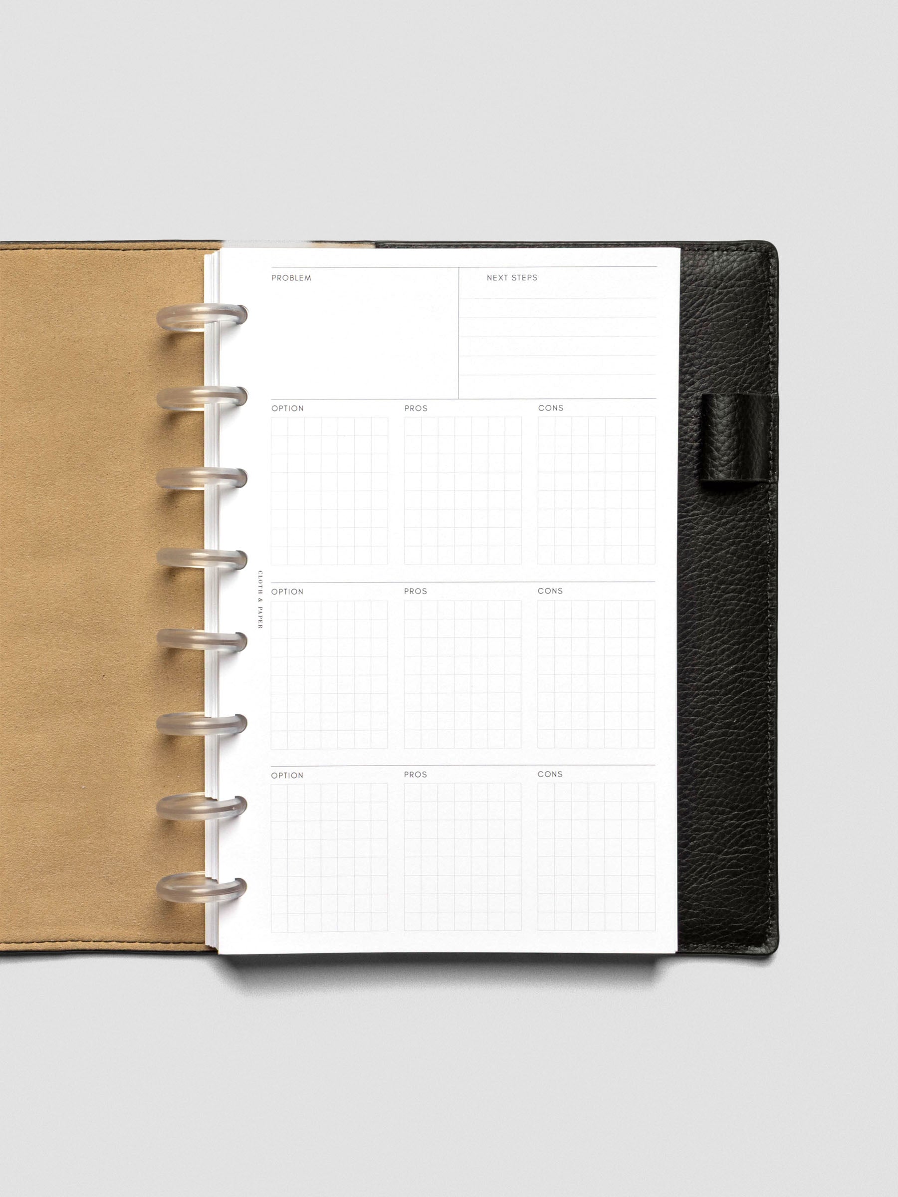 Half-letter decision-making insert displayed in a black leather planner with tan interior. The clean layout includes sections for problem, next steps, and gridded boxes for options, pros, and cons.