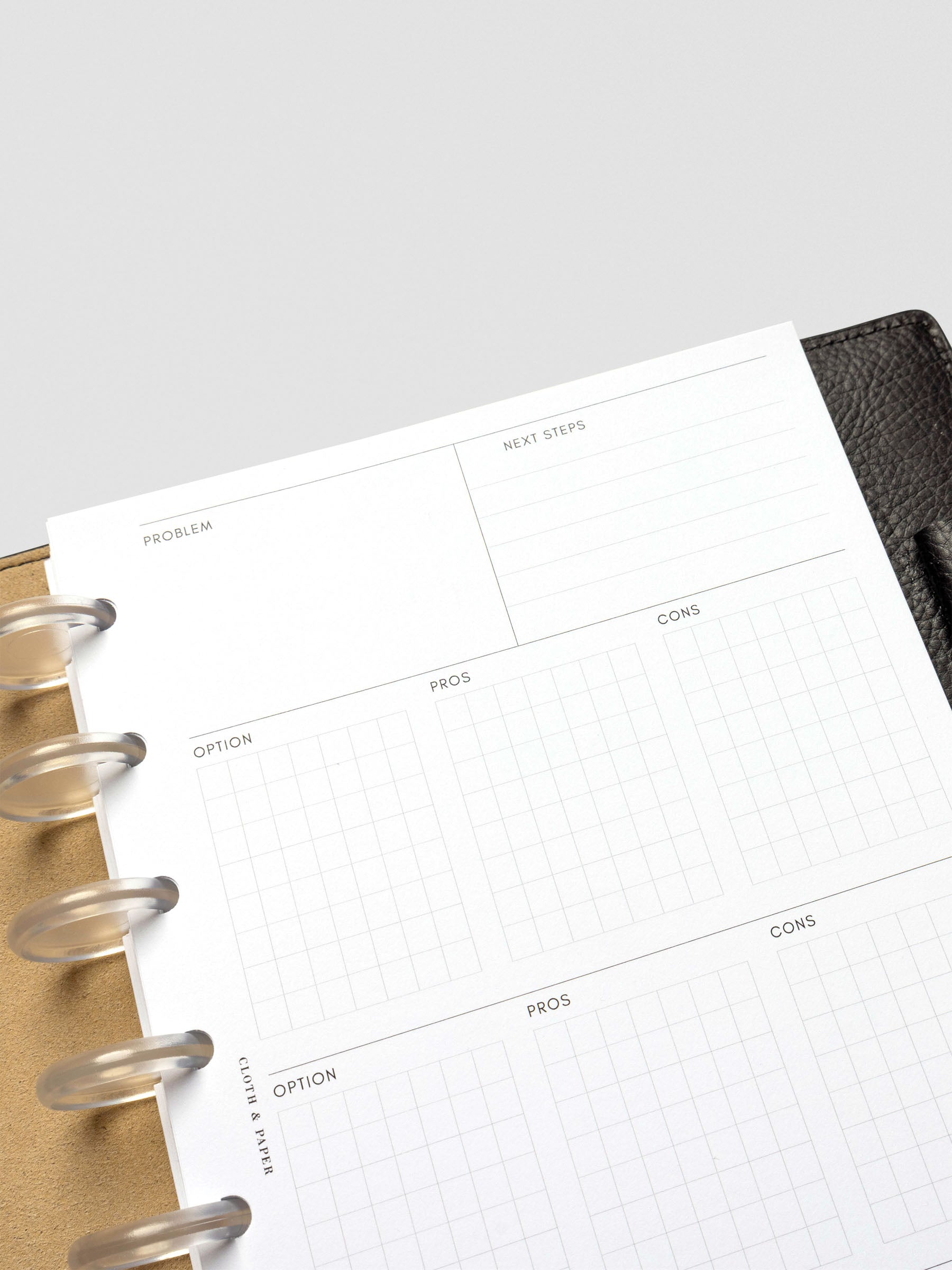 Close-up of a half-letter decision-making insert with sections for problem, next steps, and gridded boxes labeled option, pros, and cons. The page is placed in a black leather planner with tan interior and clear disc binding.