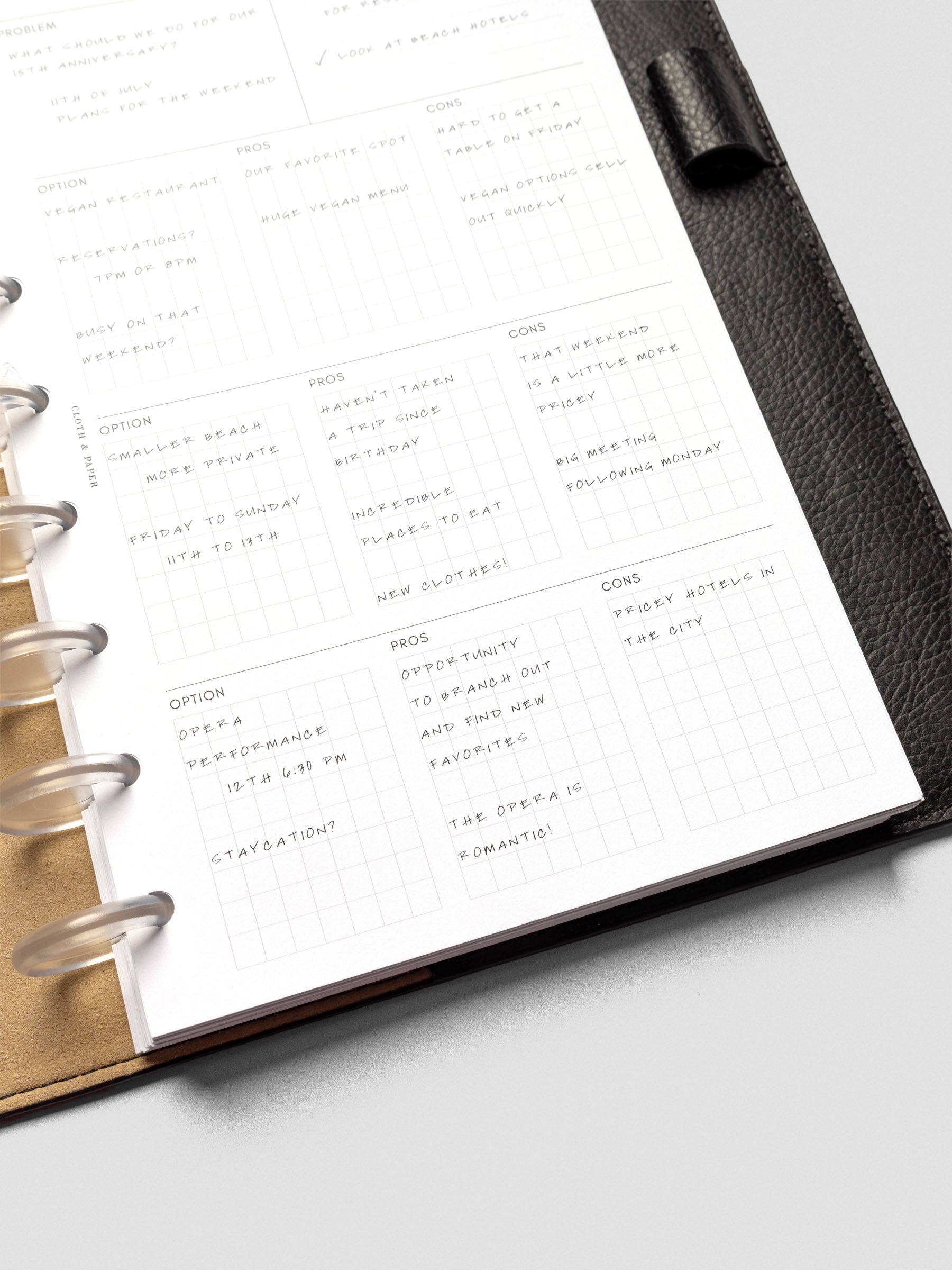 Angled view of a half-letter decision-making insert in a black leather planner, handwritten with options, pros, and cons in the gridded layout.