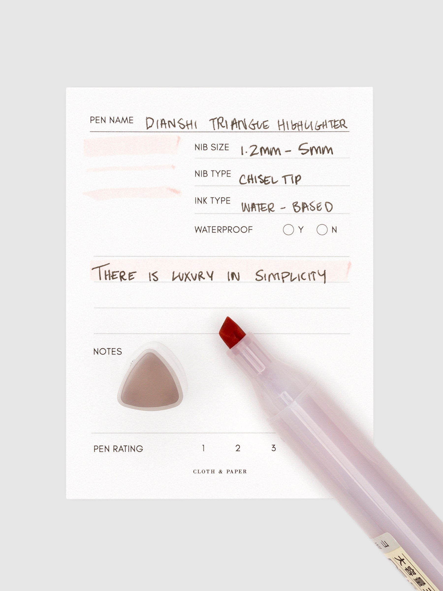 Mauve highlighter uncapped, resting on a pen test sheet displaying a writing sample detailing the highlighter's specs. The cap stands upright on the bottom left corner of the pen test sheet.