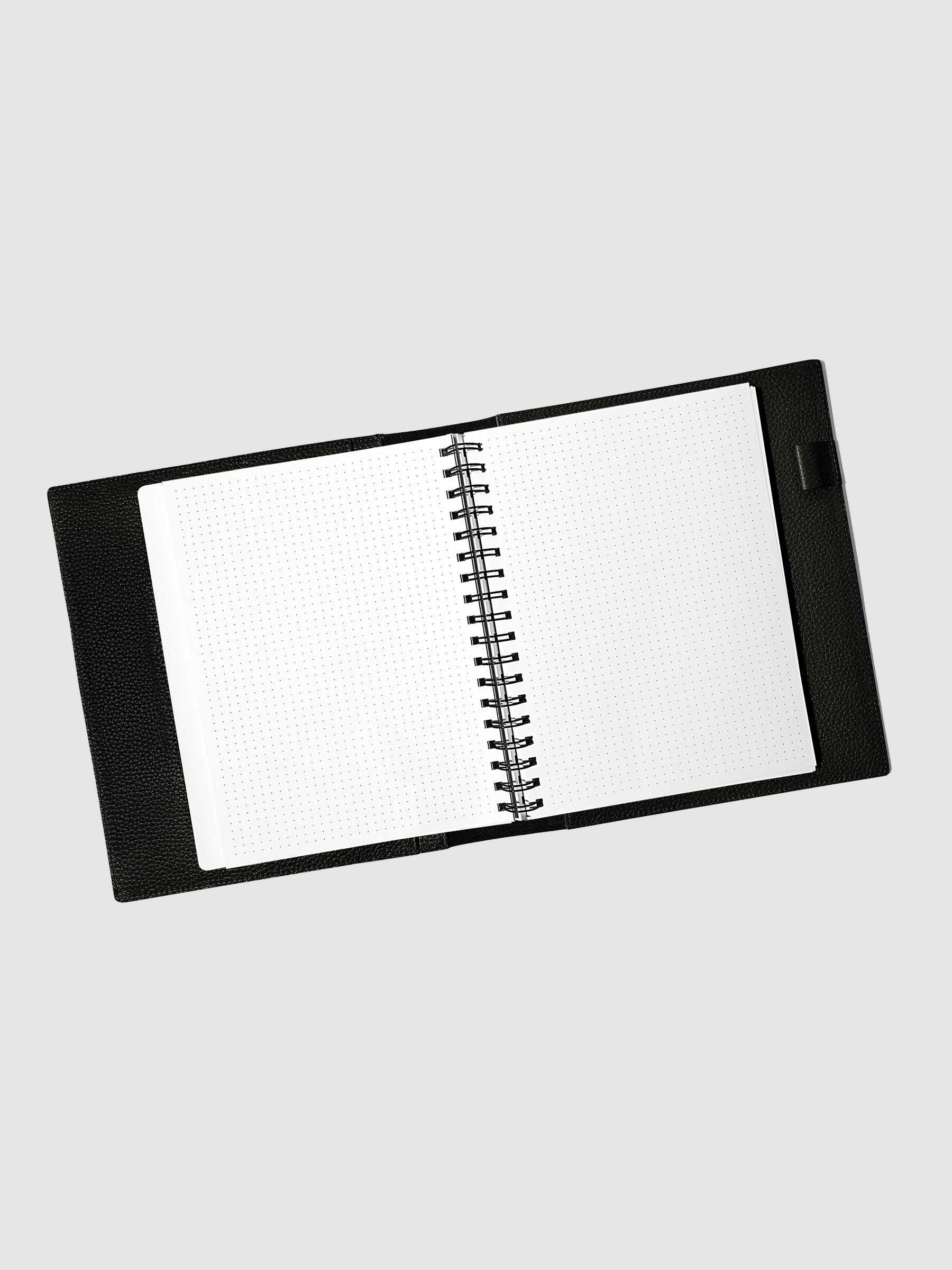 Notebook spread open inside a black leather agenda. Design shown is dot grid.