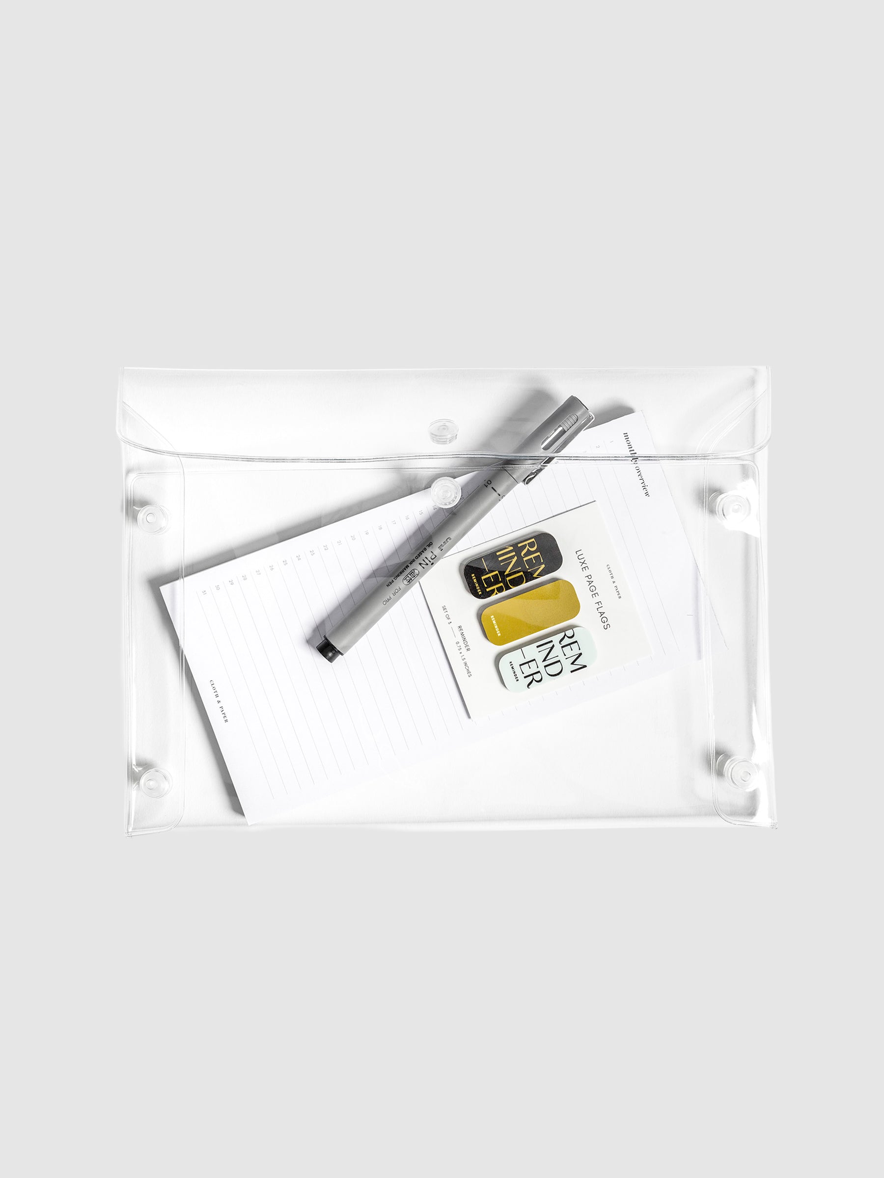 Pouch displayed filled with accessories on a neutral background. The items in the pouch are a Uni Pin Marking Pen, Monthly Overview Notepad, and Reminder Luxe Page Flags.