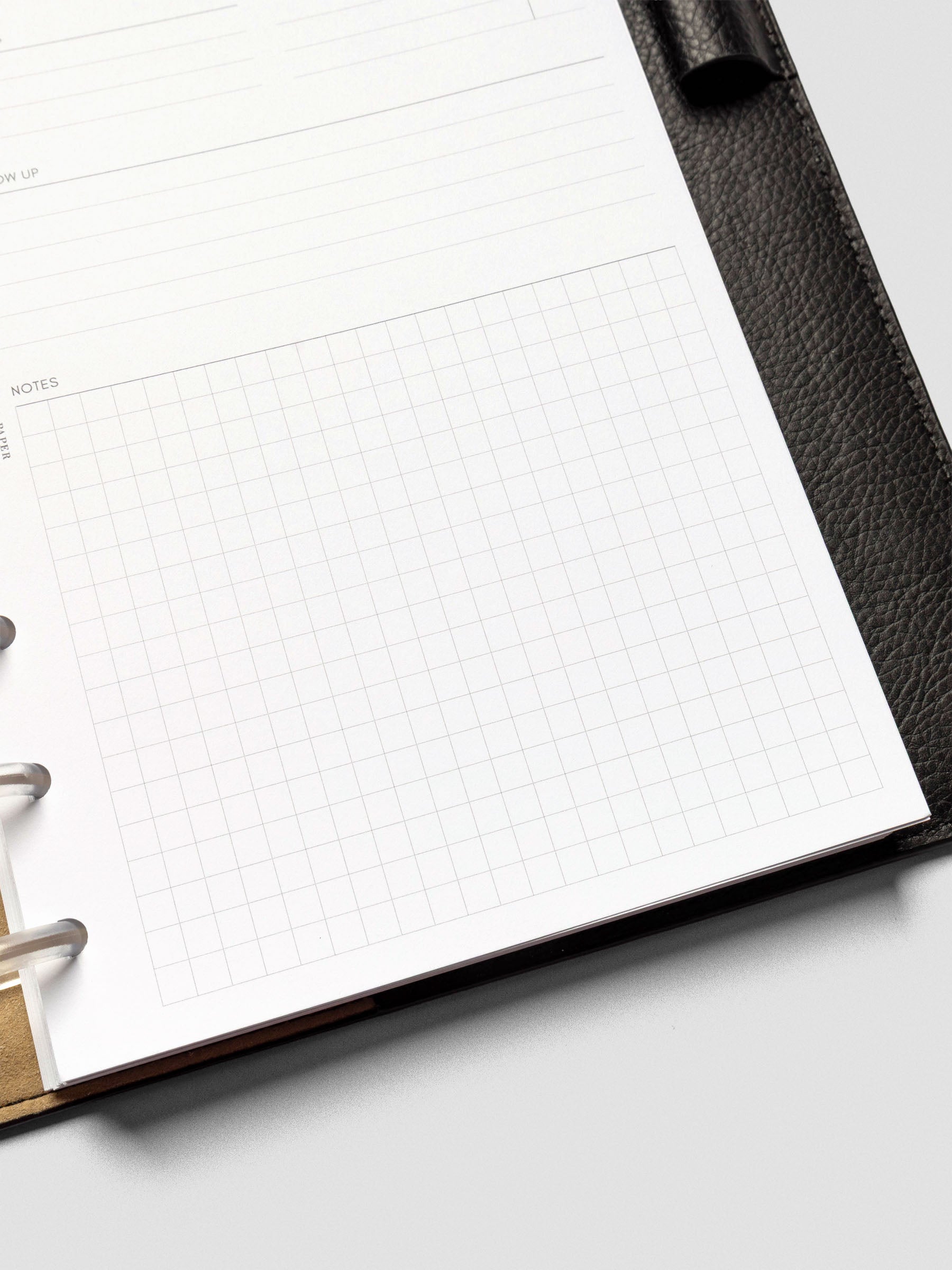 Detail view of a half-letter meeting notes insert inside a black leather planner. The page shows lined sections for follow-up and a large gridded notes area.