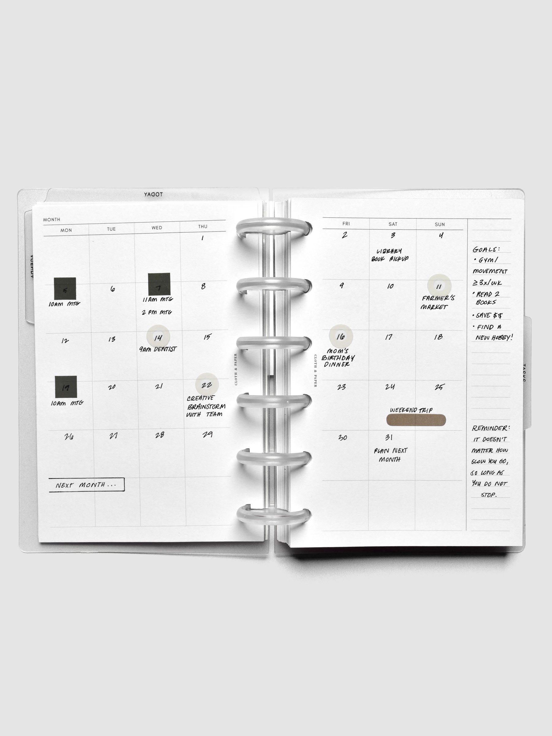 Open 6-disc planner showing a monthly calendar spread with handwritten notes and stickers.