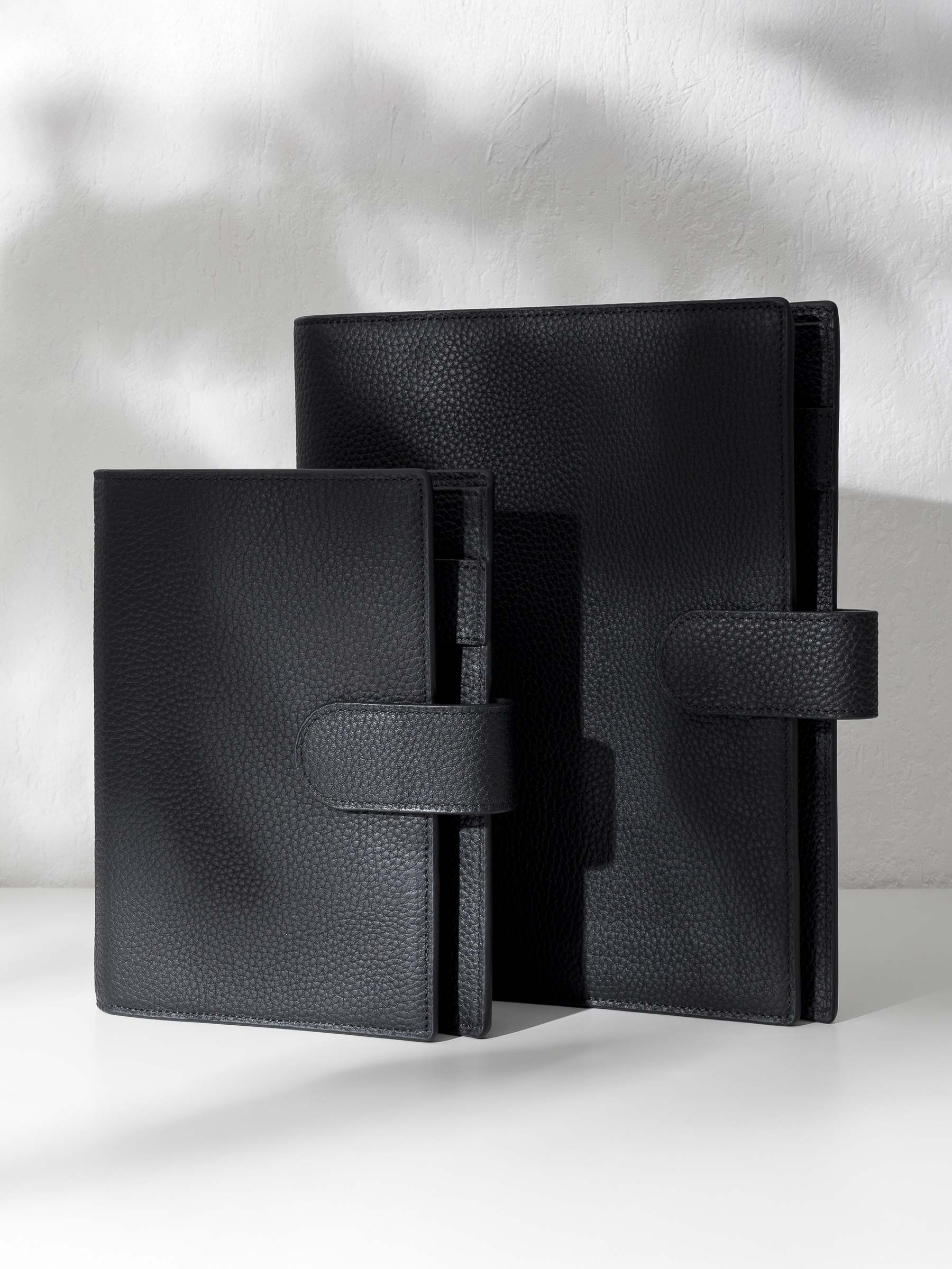 Two black leather agendas displayed against a shadowed background.